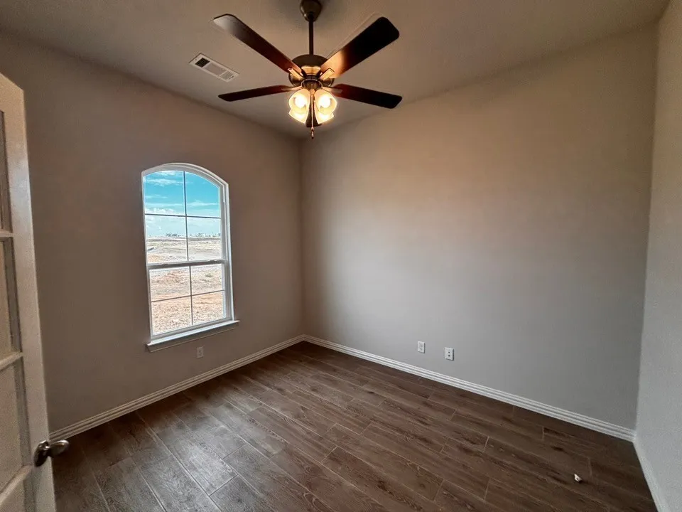 Wood-finish flooring, an arched window, a ceiling fan with integrated lighting, and a white interior door