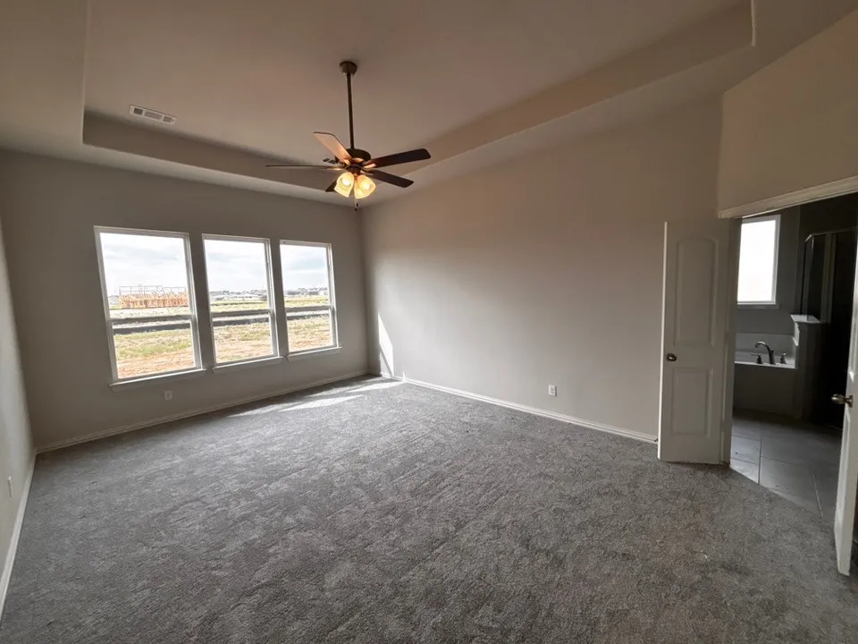 Vaulted ceiling with a ceiling fan, three large windows, light gray wall paint, and gray patterned carpeting