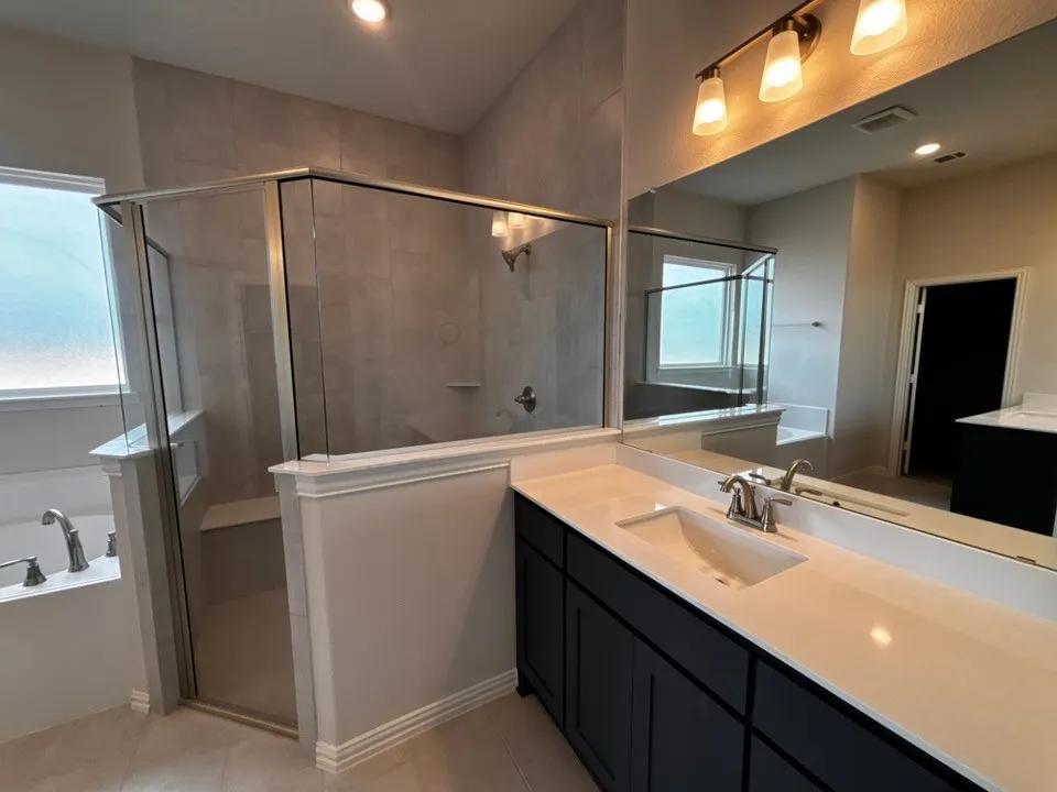 Spacious bathroom featuring a glass-enclosed shower, a separate built-in tub, a double vanity with a light-colored countertop, and a large mirror