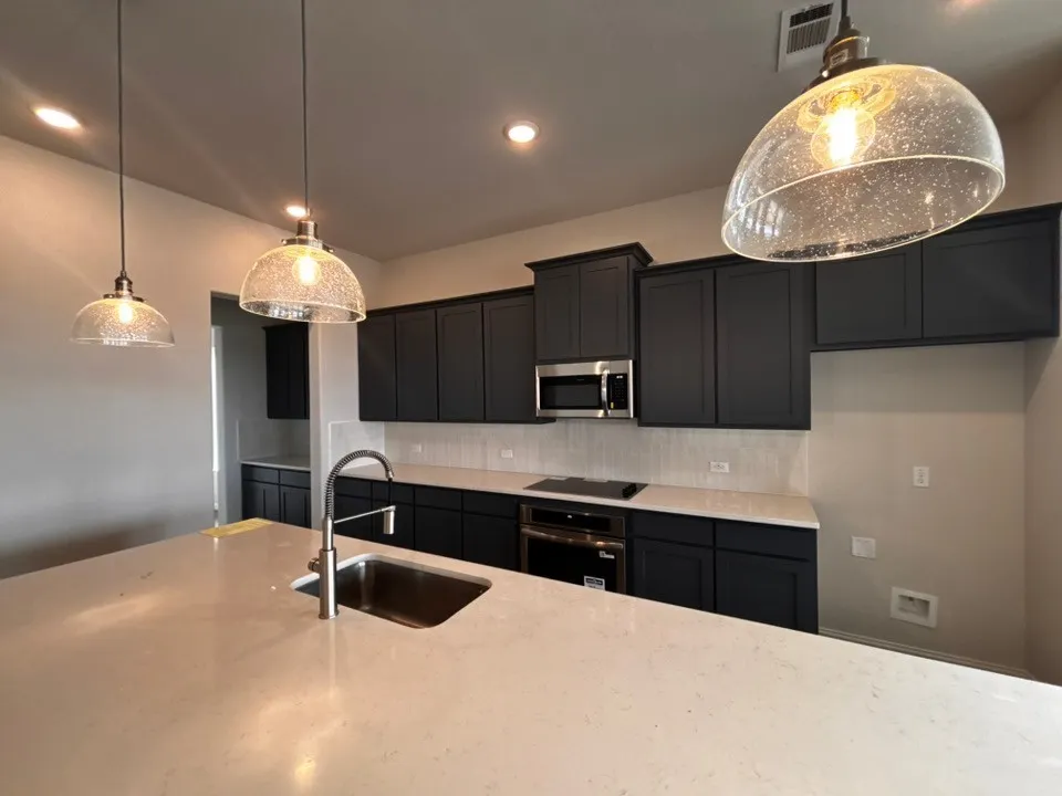 Kitchen featuring a large island with an undermount sink, quartz countertops, dark cabinetry, stainless steel appliances, and pendant lighting