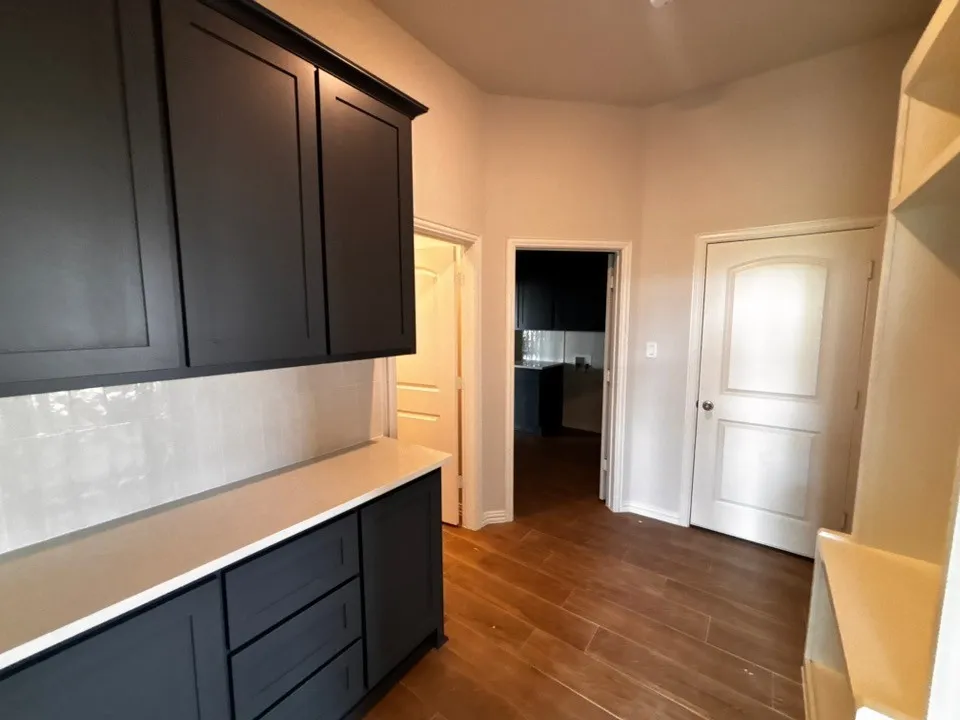 Dark-toned cabinetry with a light-toned countertop, subway tile backsplash, and wood-finish flooring