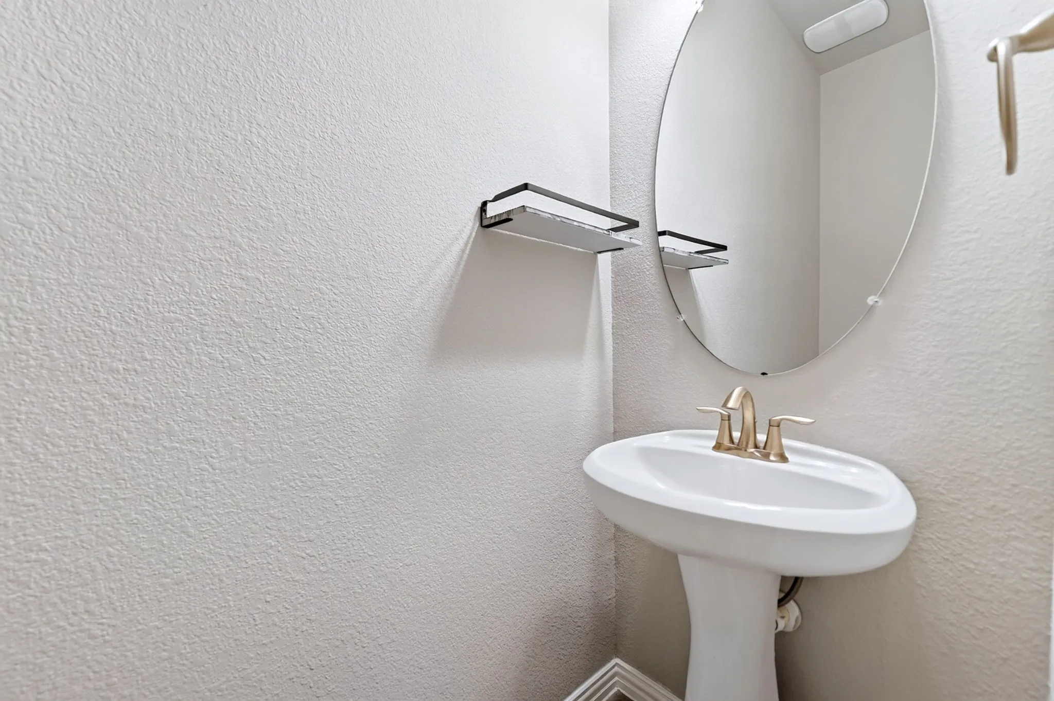Pedestal sink with a brushed nickel faucet, oval mirror, and wall-mounted shelving