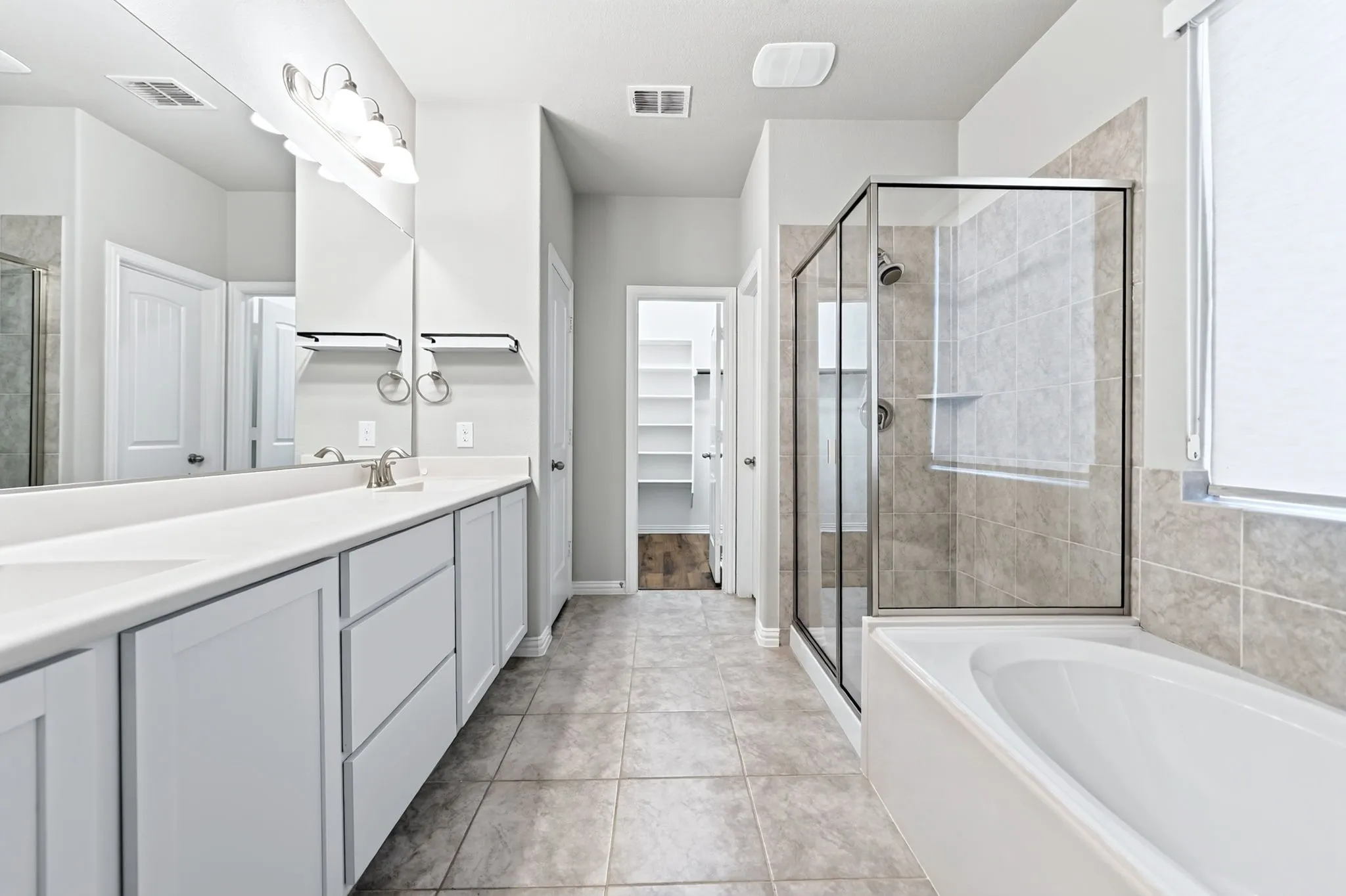 Dual vanity with white cabinetry and integrated sinks, a walk-in shower with glass enclosure, a separate built-in bathtub, and ceramic tile flooring