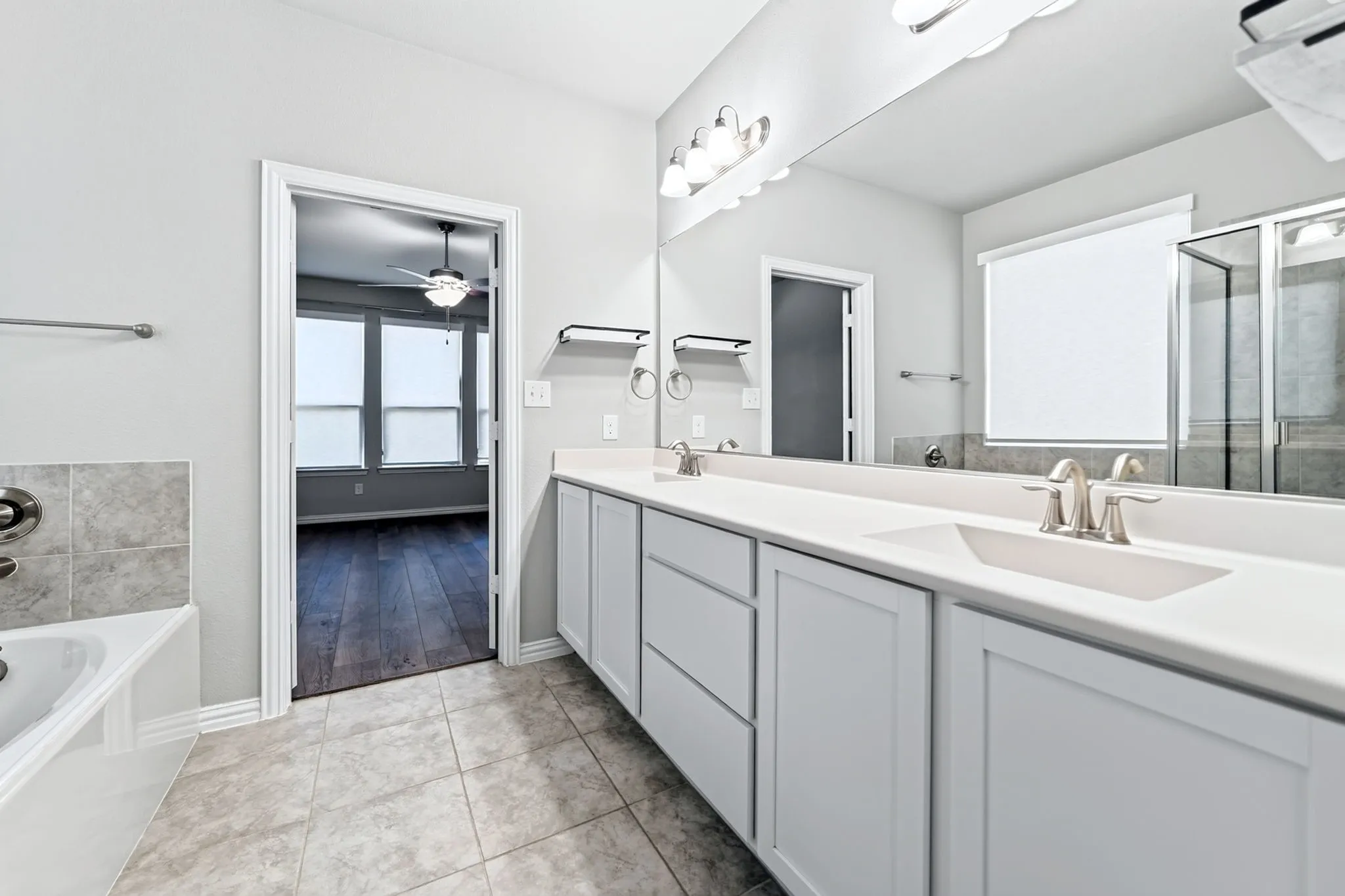 Dual vanity with white cabinetry and integrated sinks, a built-in tub with tile surround, and a walk-in shower with a glass enclosure