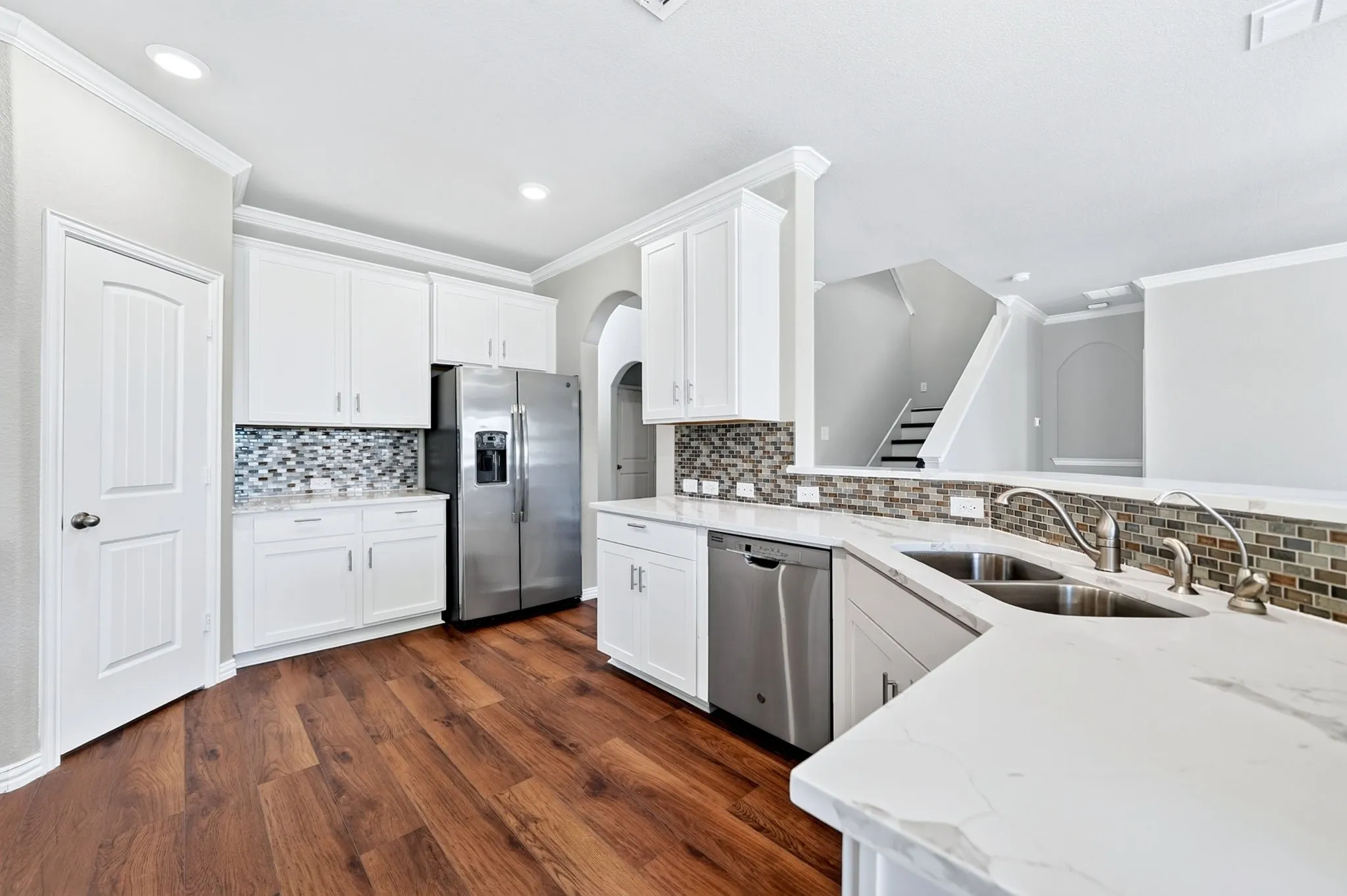 White cabinetry, stainless steel appliances, wood-finish flooring, mosaic tile backsplash, and solid surface countertops