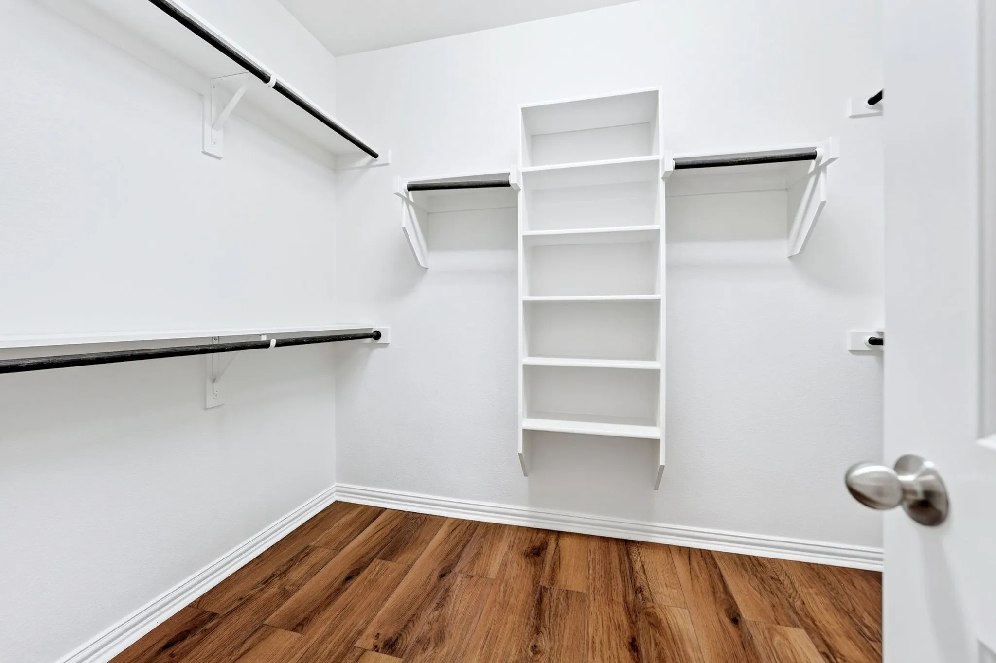 Built-in shelving, multiple clothing rods, wood-finish flooring, and white walls