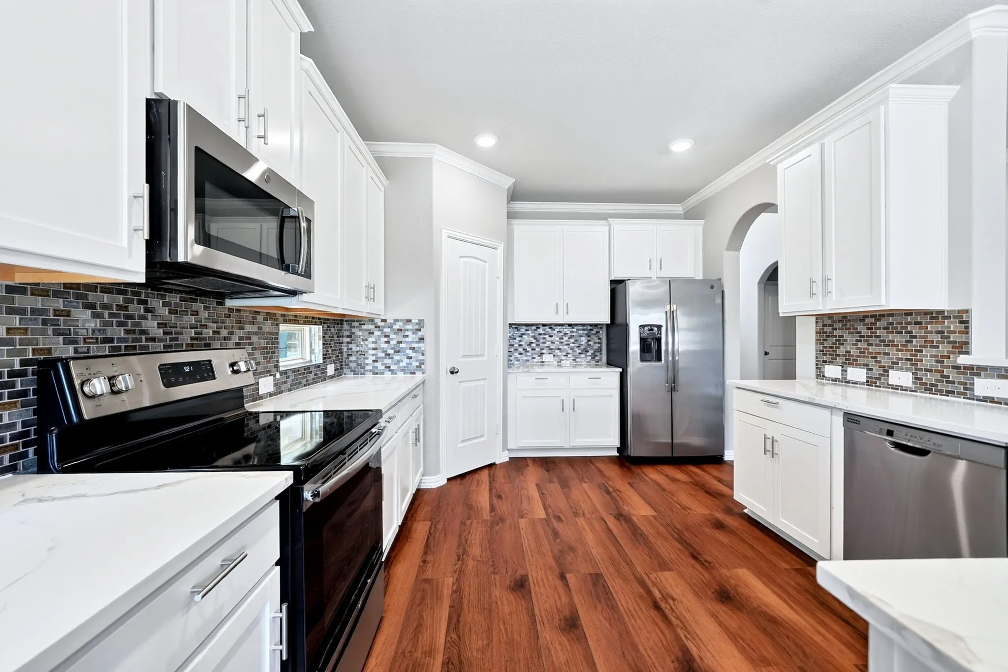 Kitchen featuring wood-finish flooring, white cabinetry, integrated stainless steel appliances, mosaic tile backsplash, and light-toned countertops