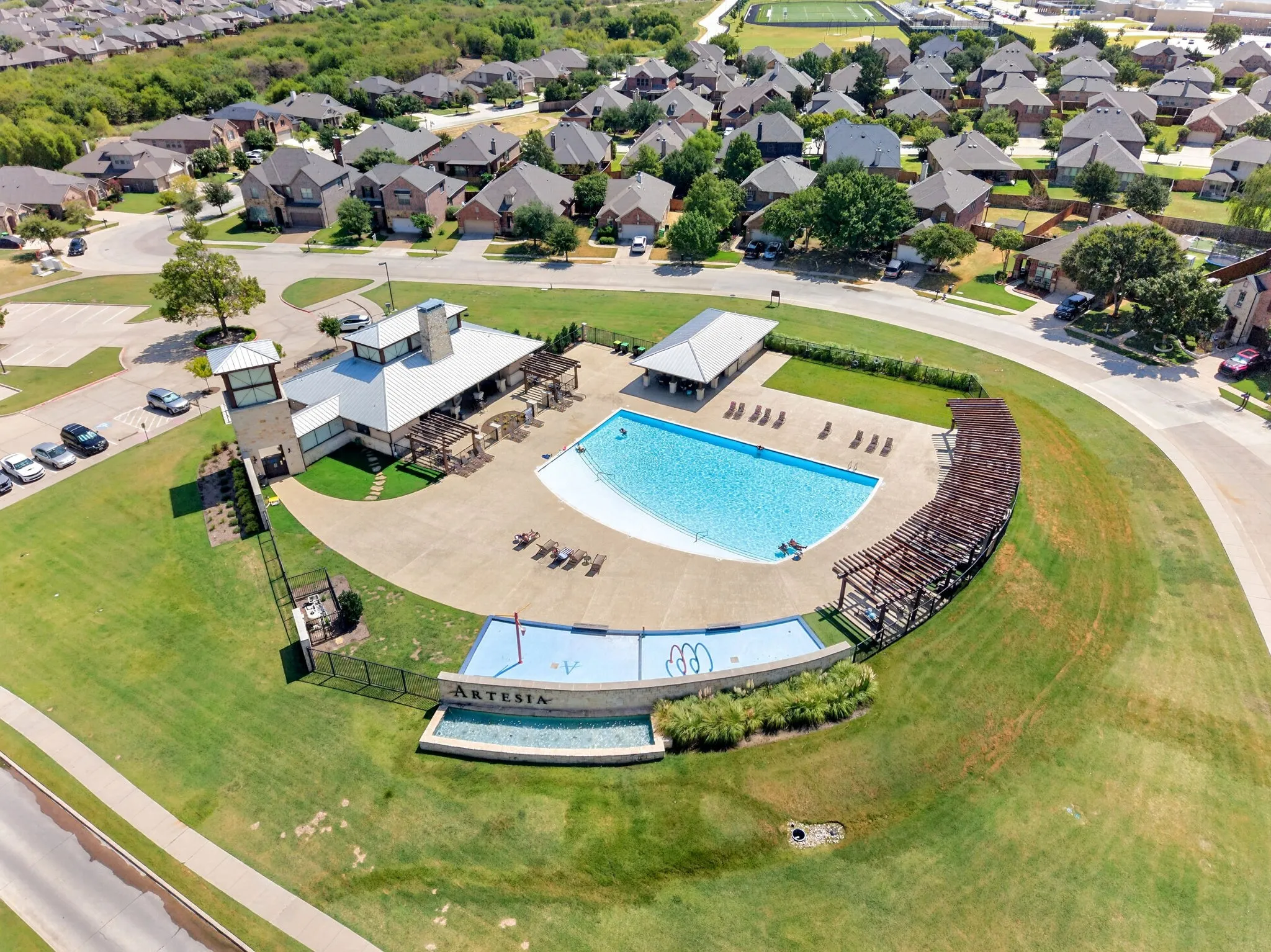 Community amenity center featuring a swimming pool, shaded lounge areas, and an entry monument