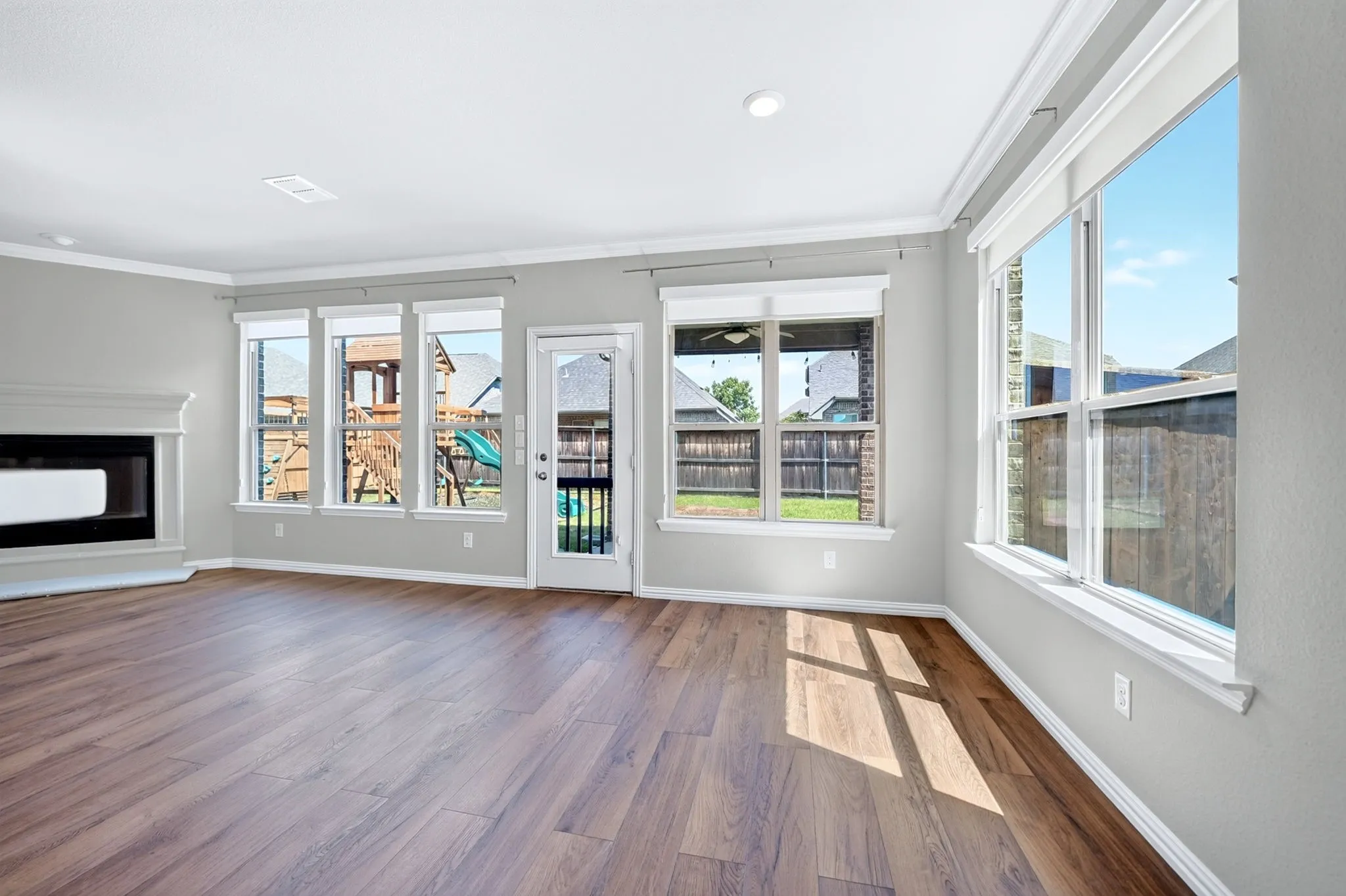 Wood-finish flooring, white crown molding, recessed lighting, and a fireplace with a white mantel and hearth