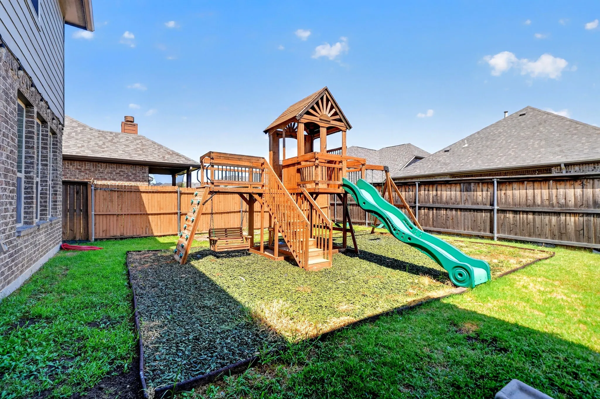 Expansive backyard featuring a wood-finish play structure, green slide, and manicured lawn