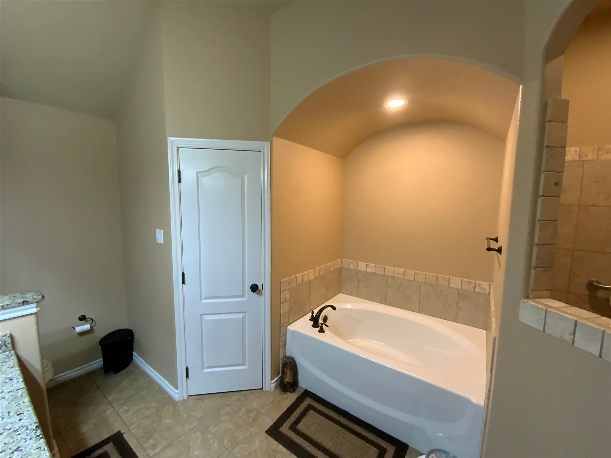 Recessed tub with bronze-finish fixtures, arched alcove, and tile surround