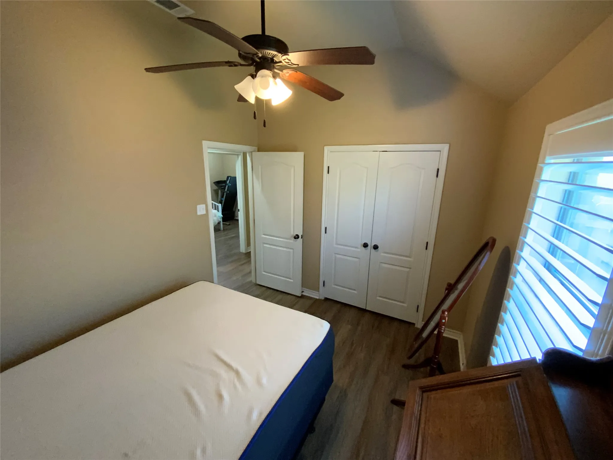 Vaulted ceiling featuring a ceiling fan with light fixture, wood-finish flooring, plantation shutters, and double closet doors