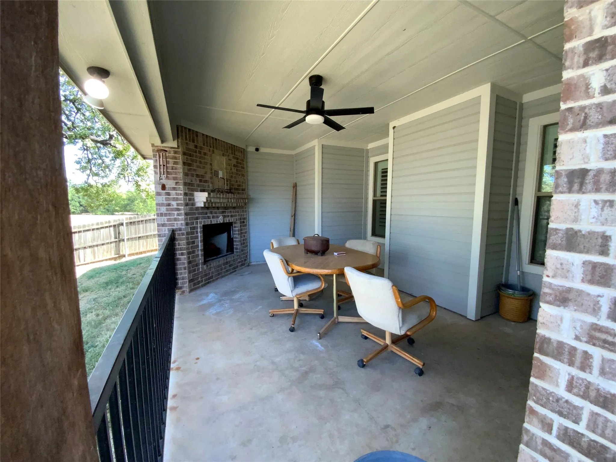 Covered patio with a brick fireplace, concrete flooring, exterior ceiling fan, and horizontal siding