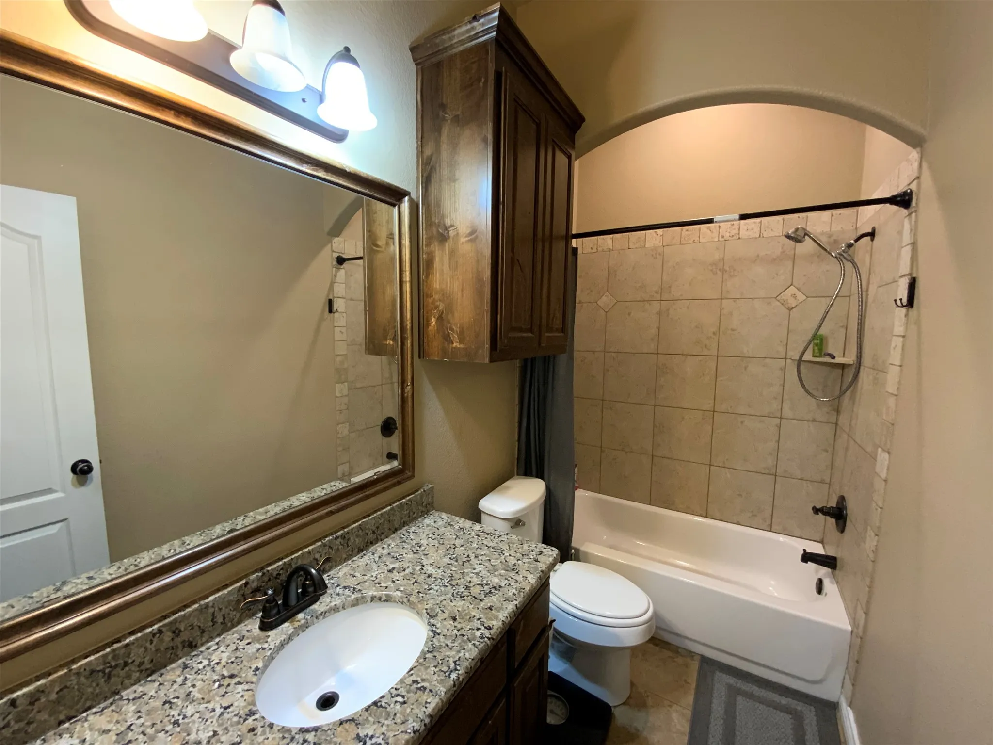 Granite-look countertop, wood-finish vanity with an integrated sink, full-width mirror, tile shower surround, and a built-in shower niche