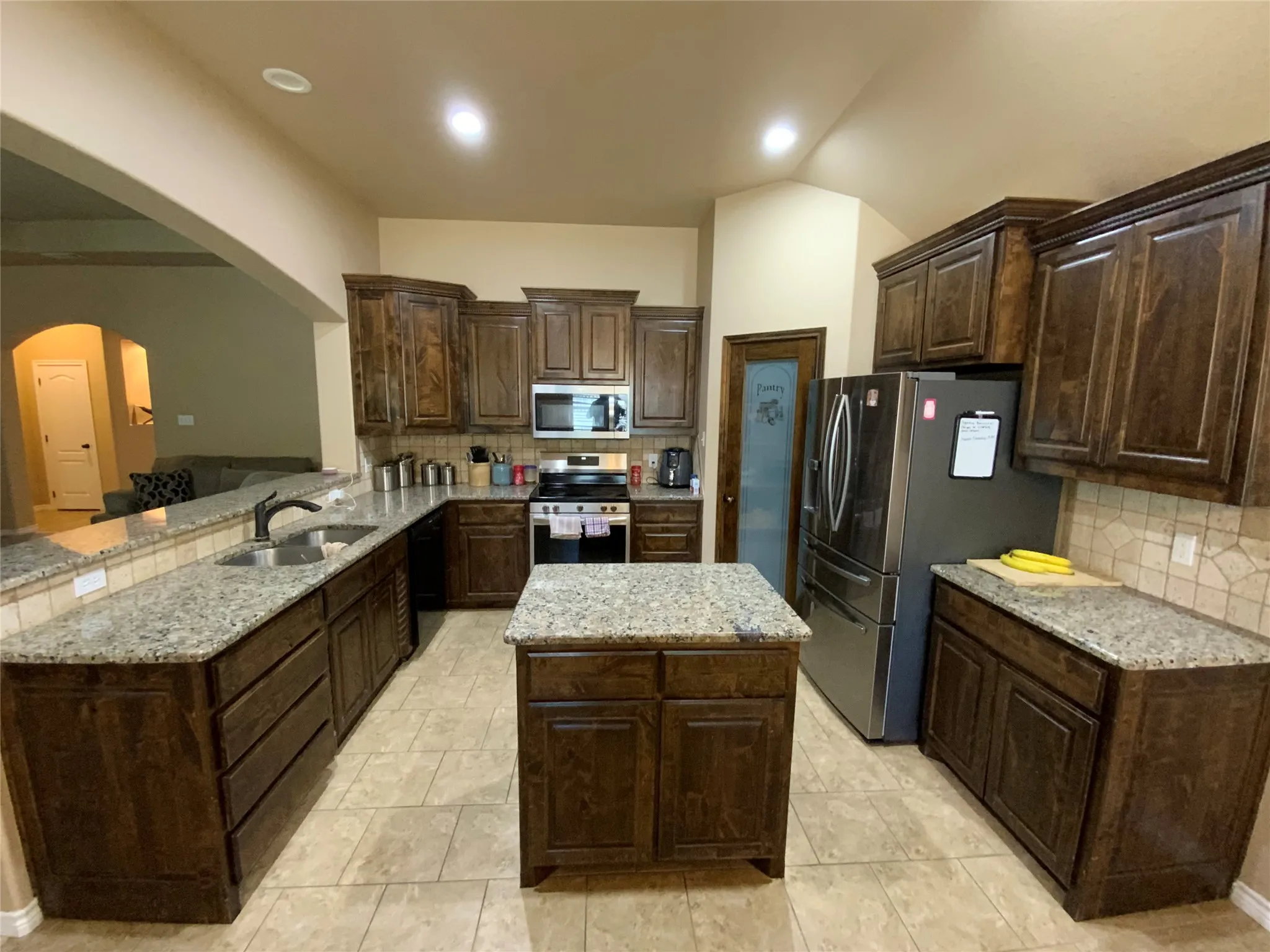 Kitchen featuring a central island, granite countertops, tile flooring, rich wood-finish cabinetry, and stainless steel appliances