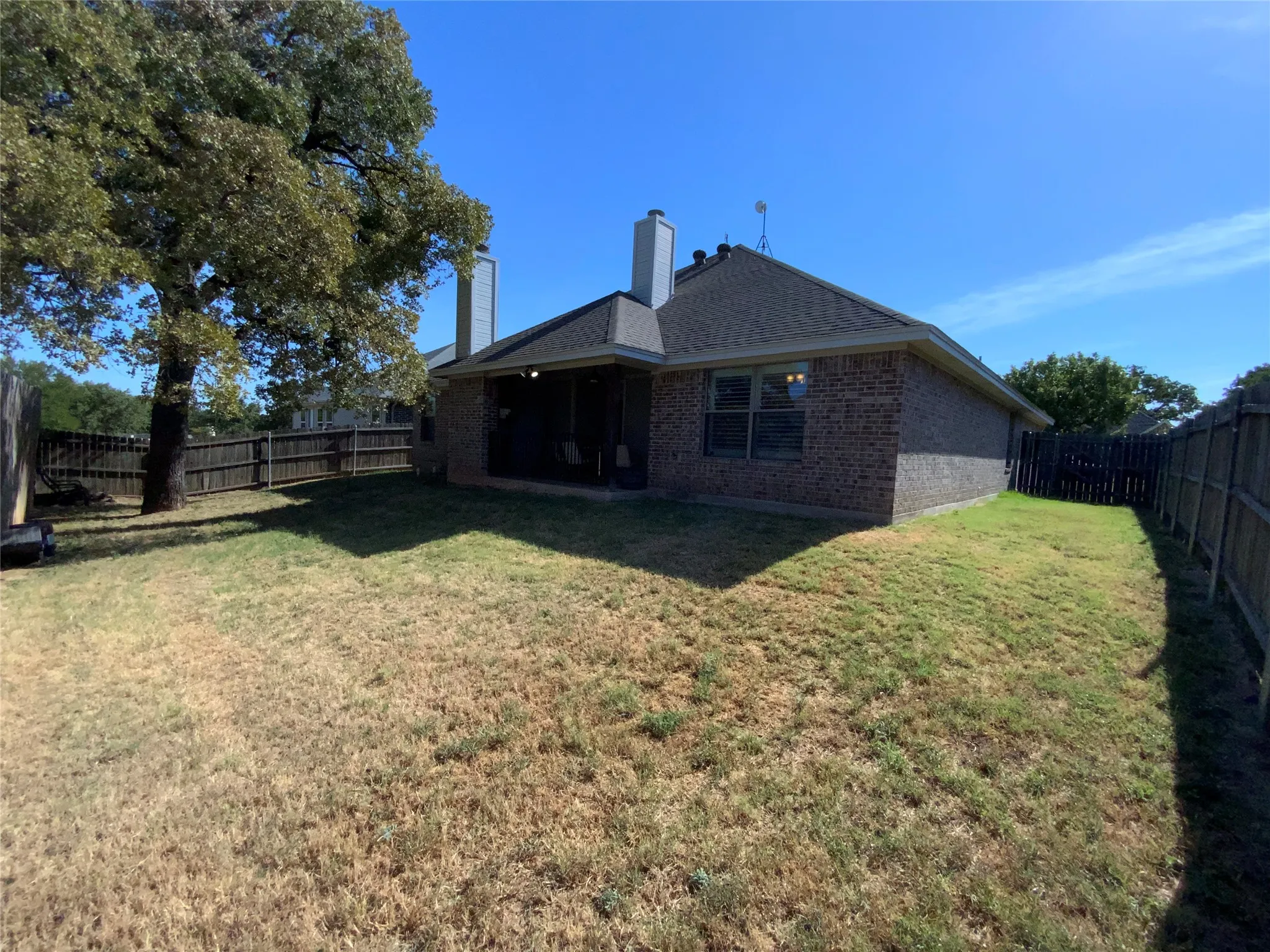 Brick exterior with a covered patio, a fenced yard, and a mature tree