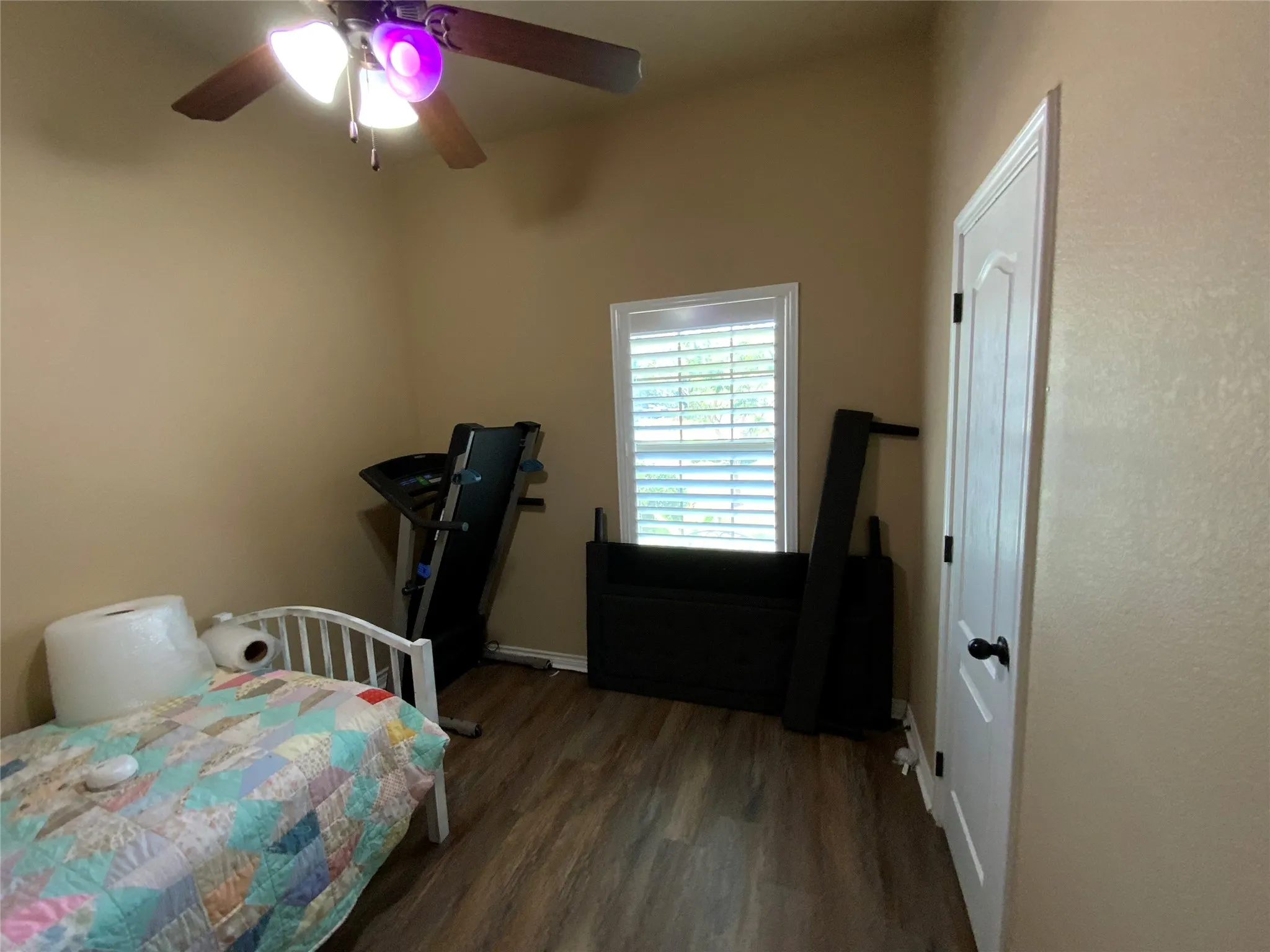 Vaulted ceiling, wood-finish flooring, ceiling fan with integrated lighting, window with plantation shutters, white interior door with black hardware