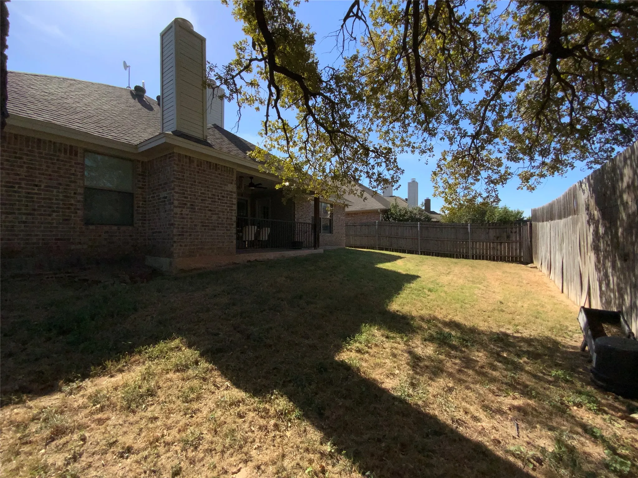Brick exterior featuring a covered patio, a fenced backyard, and mature trees