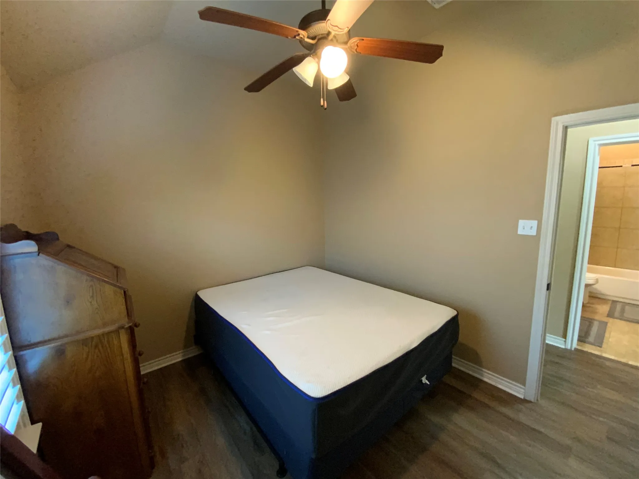 Vaulted ceiling with an attached ceiling fan, wood-finish flooring, and a doorway opening to a tiled bathroom