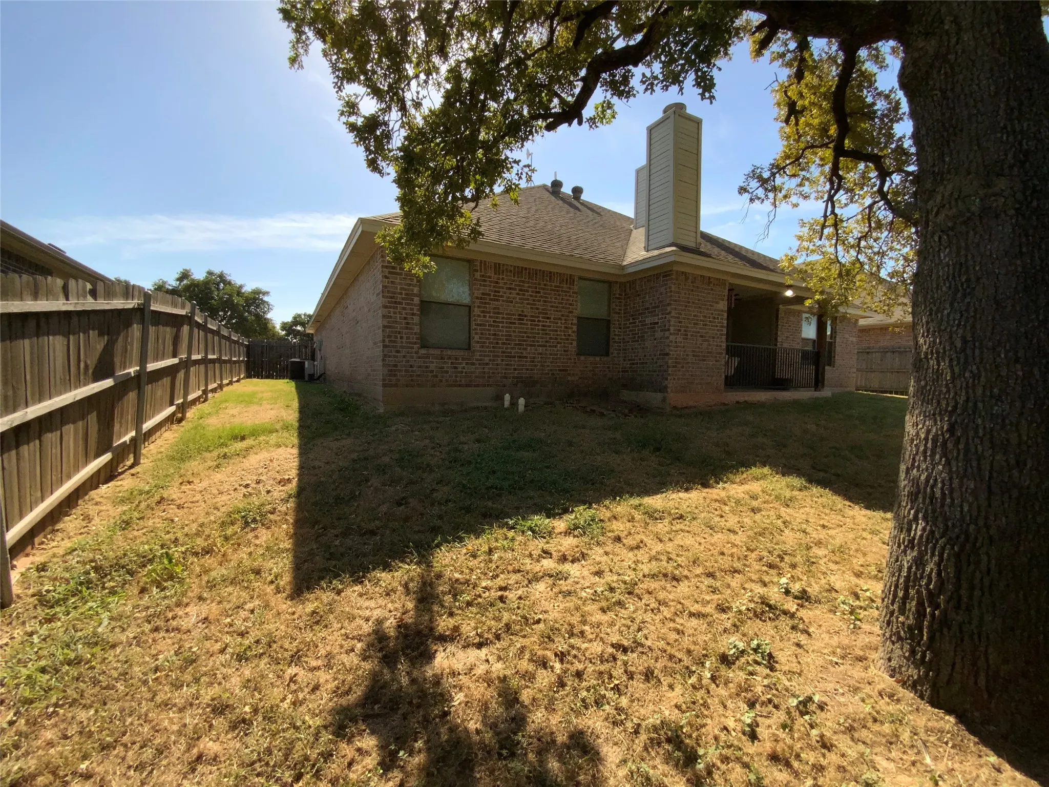 Brick exterior with a covered patio, wood fencing, and a mature tree