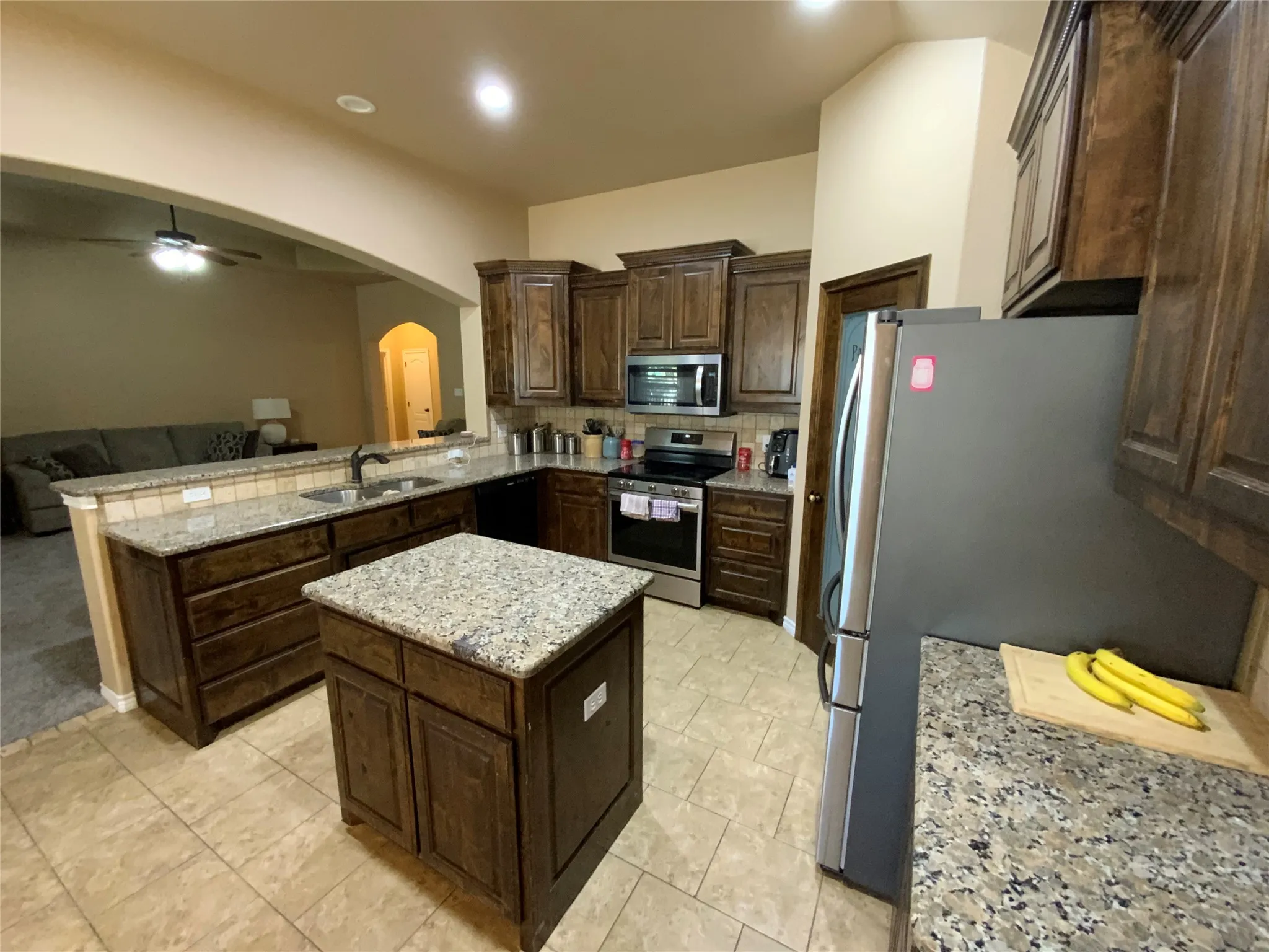 Kitchen featuring dark wood cabinetry, light-toned tile flooring, light-toned speckled countertops, and a central island
