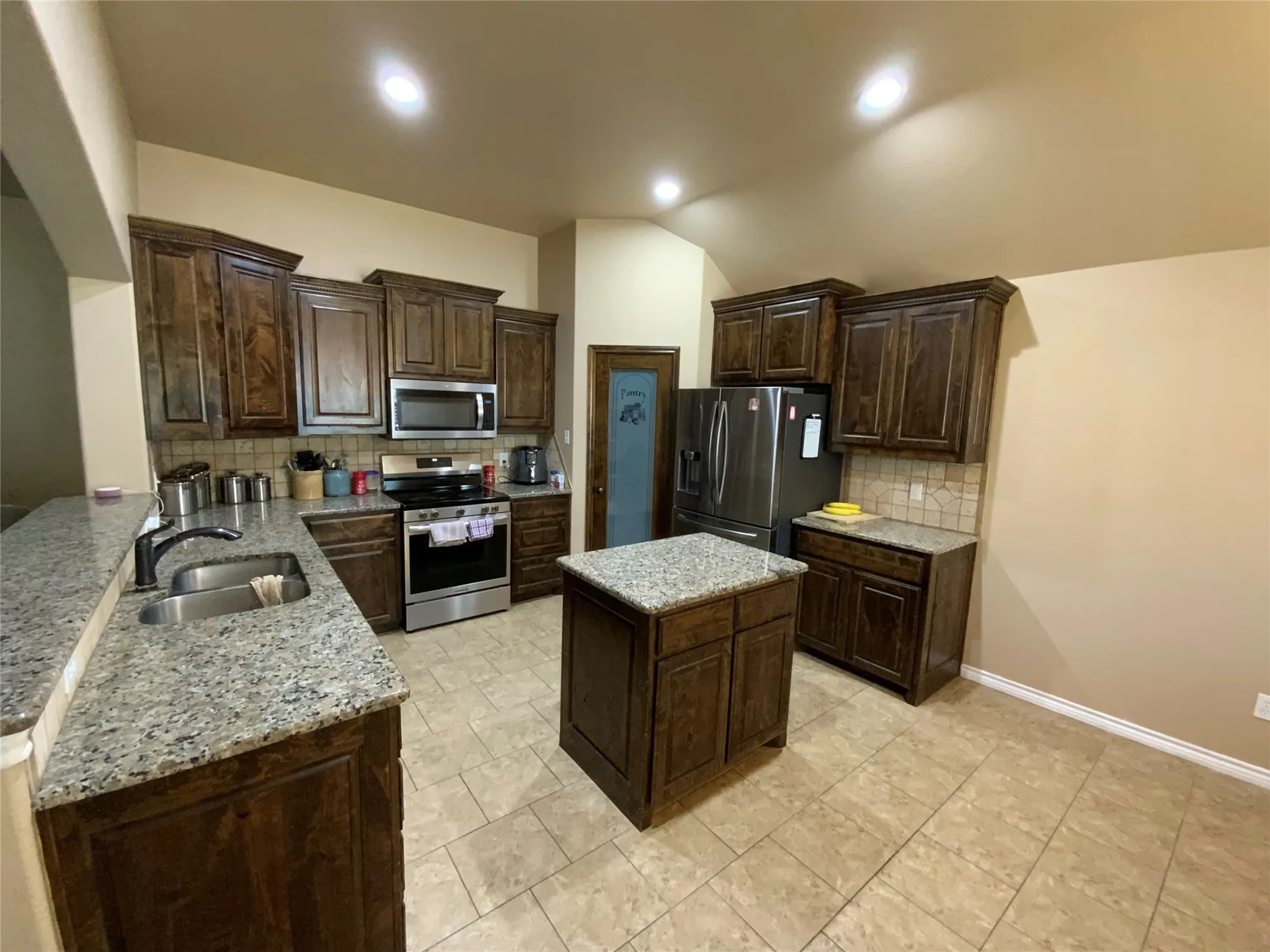 Kitchen featuring rich wood-finish cabinetry, granite countertops, a central island, and stainless steel appliances