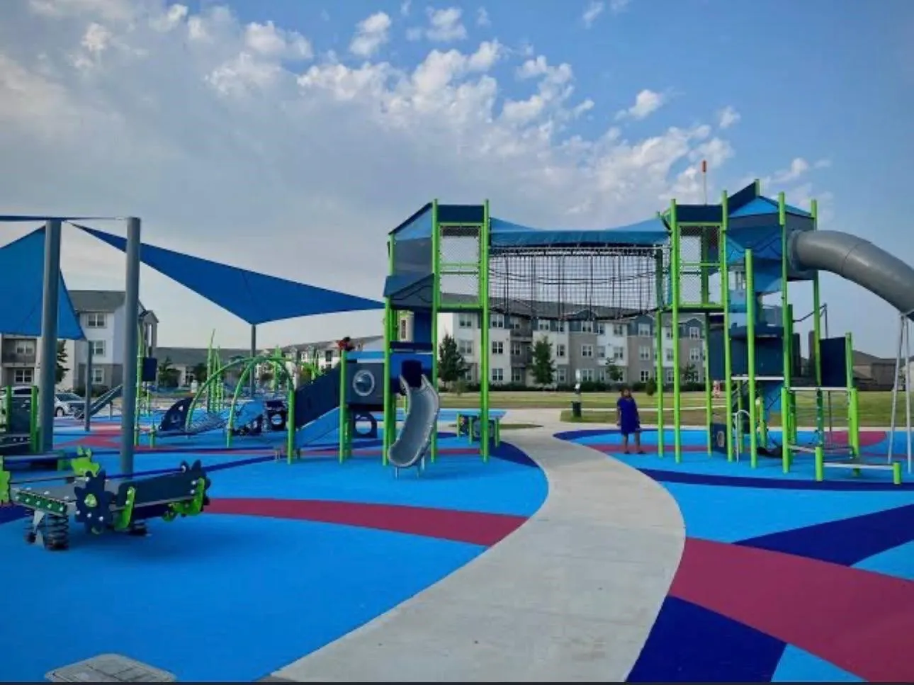 Integrated playground featuring multiple slides, climbing structures, shade sails, and a patterned soft-fall surface