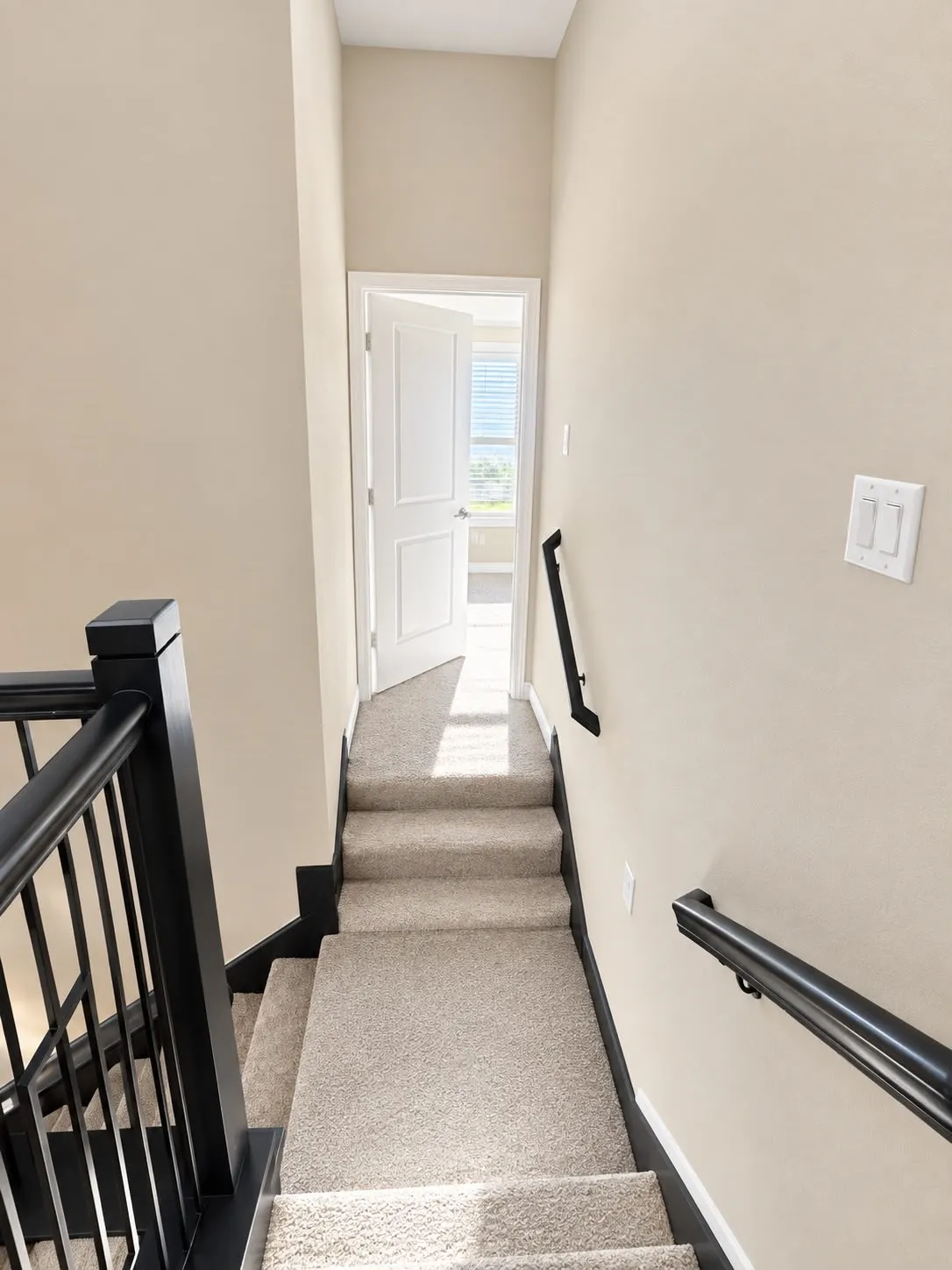 Carpeted stairs with black handrails and balusters, leading to an open doorway