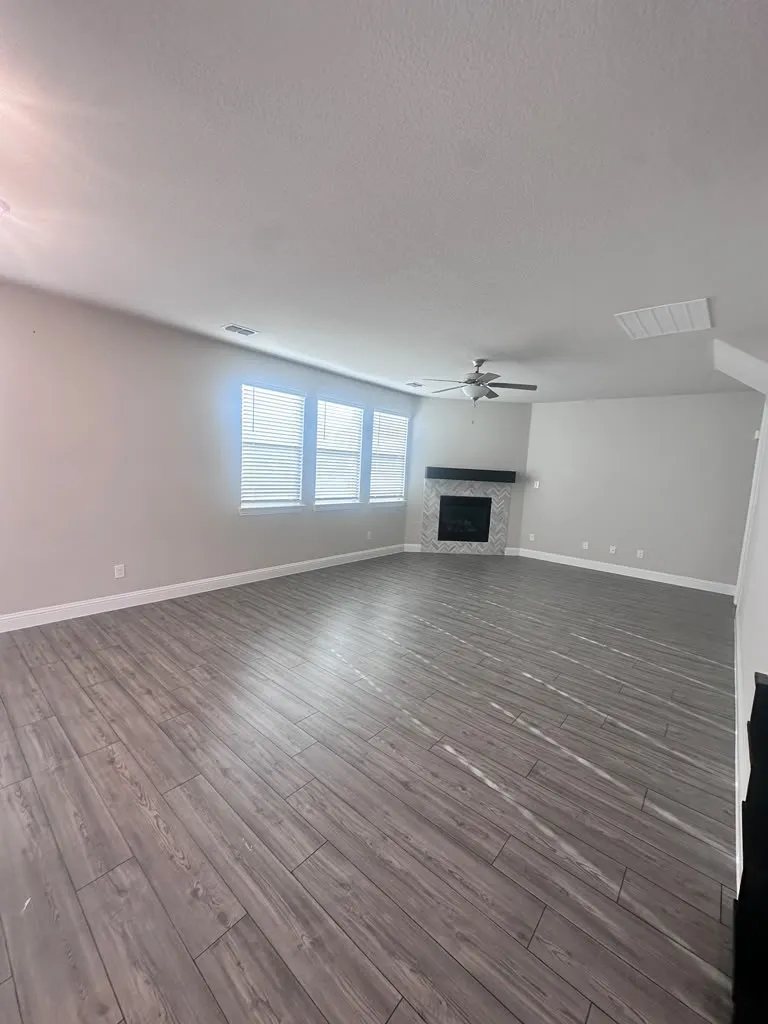 Spacious interior with wood-finish flooring, multiple windows with blinds, a ceiling fan, and a fireplace with a mantel