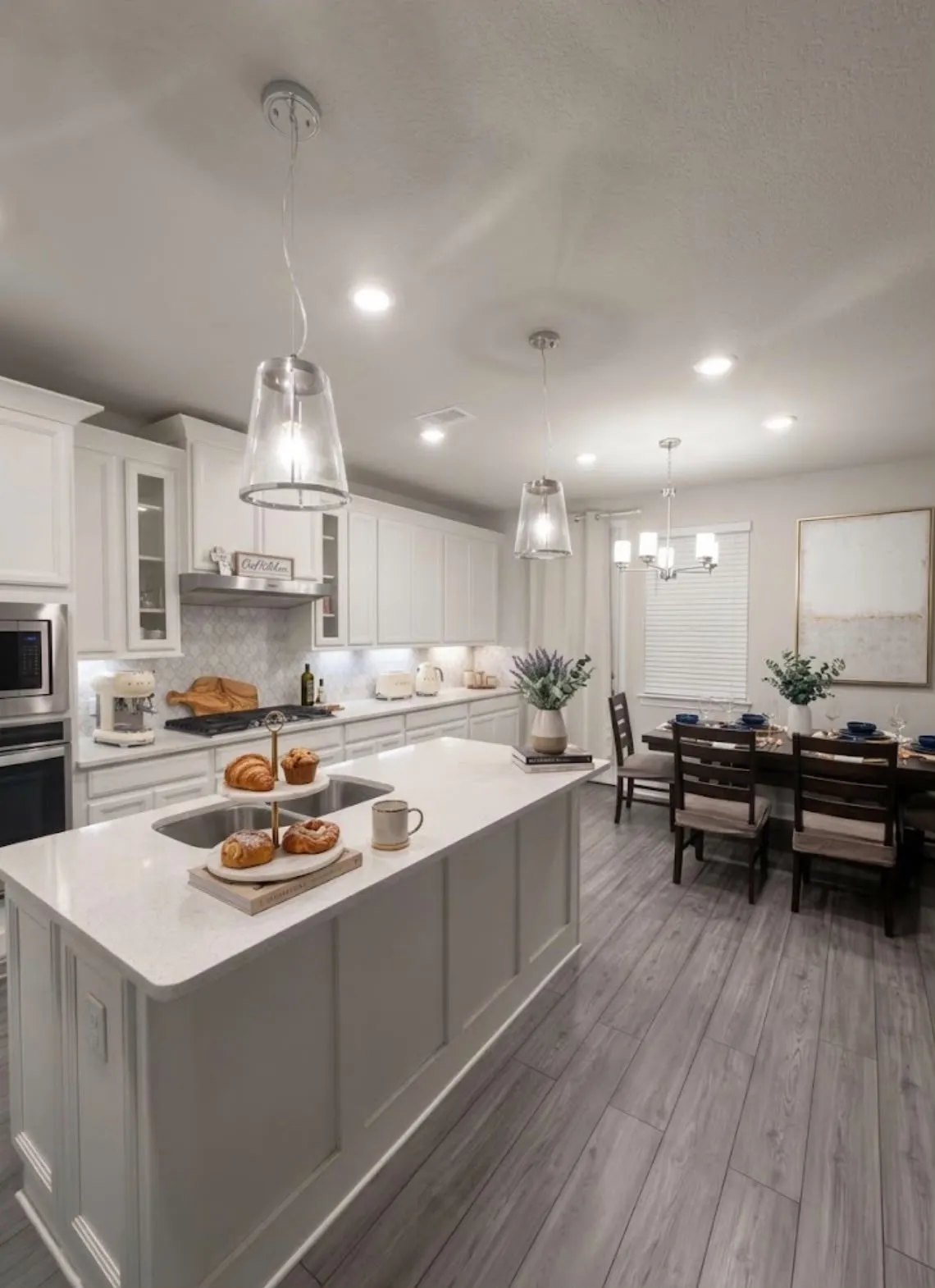 Kitchen with a large island featuring an undermount sink and light-toned countertop, white cabinetry, stainless steel appliances, and a tile backsplash