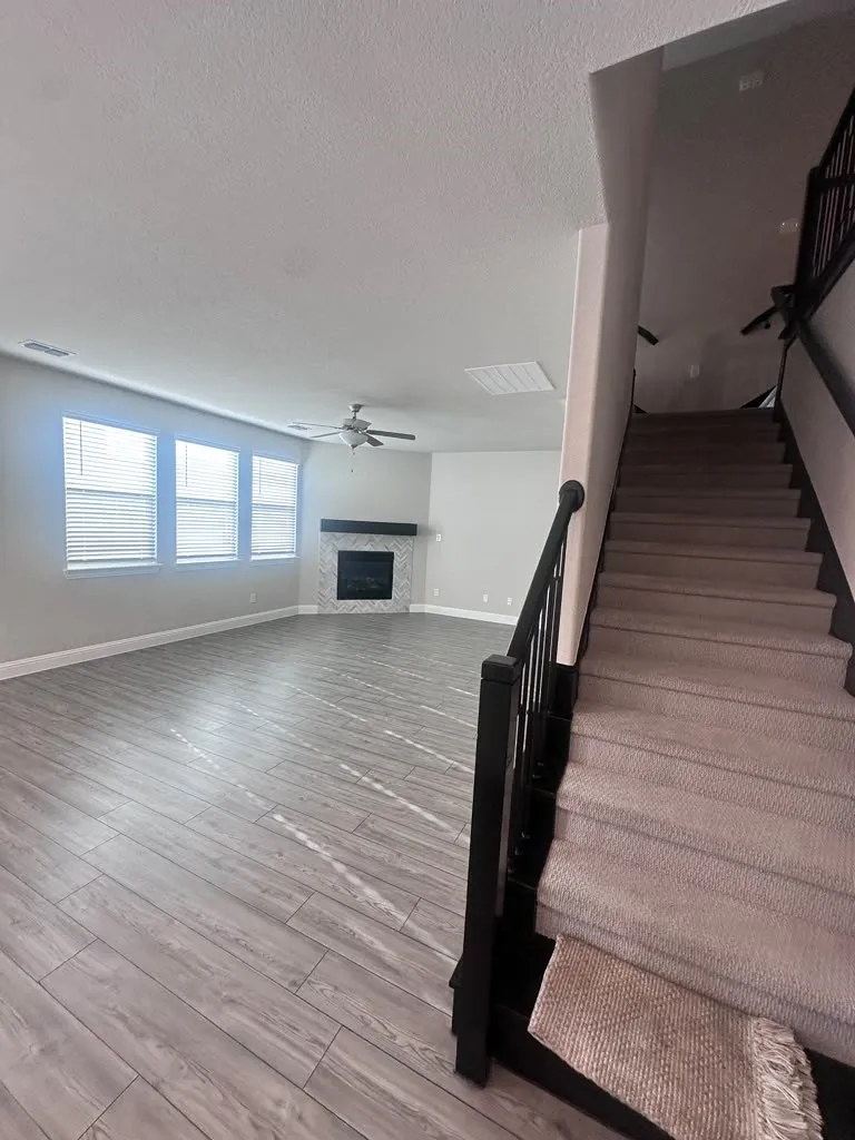 Expansive living area featuring wood-finish flooring, a ceiling fan, and multiple windows with blinds