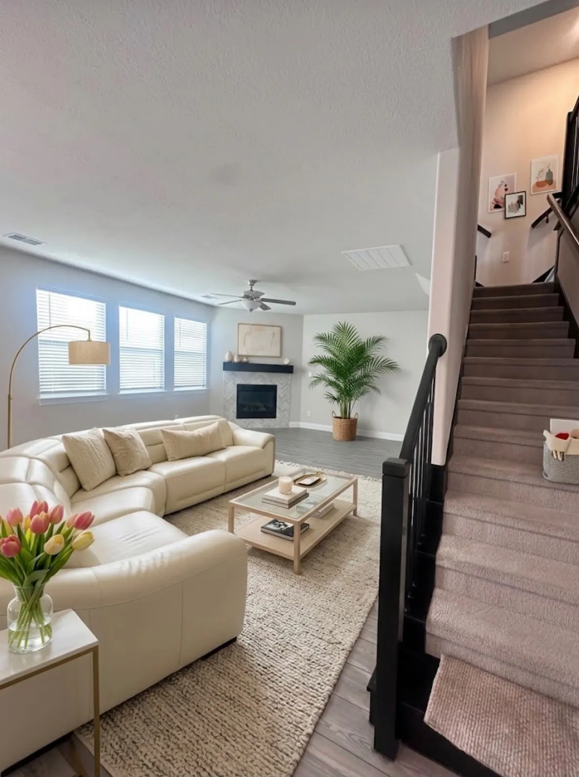 Open concept living area featuring wood-finish flooring, multiple windows with blinds, a modern ceiling fan, and a fireplace with a dark mantel