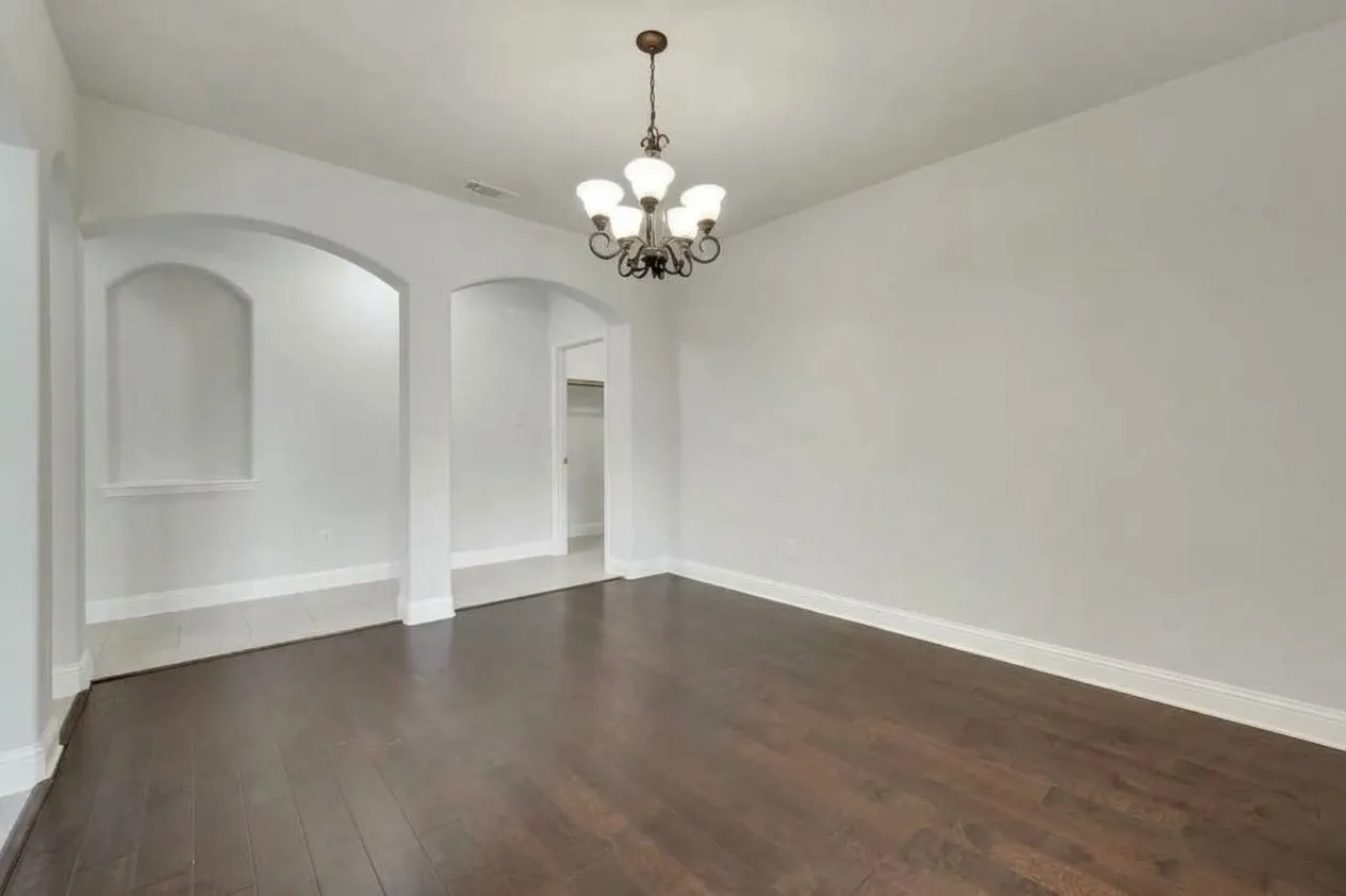 Dark wood-finish flooring, arched doorways, a decorative wall niche, and a bronze chandelier