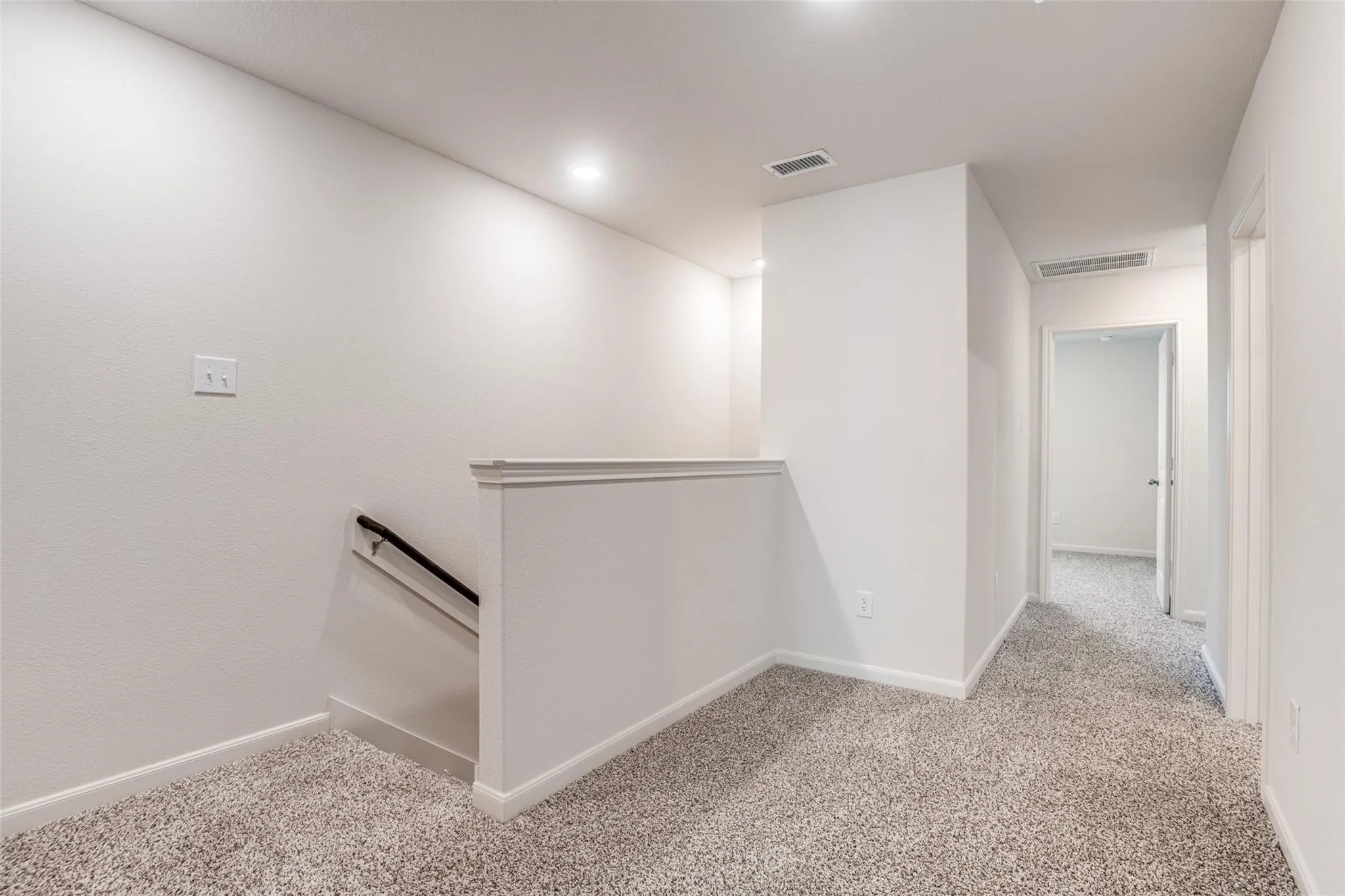 Carpeted landing with white walls, recessed lighting, and a white balustrade with a black handrail