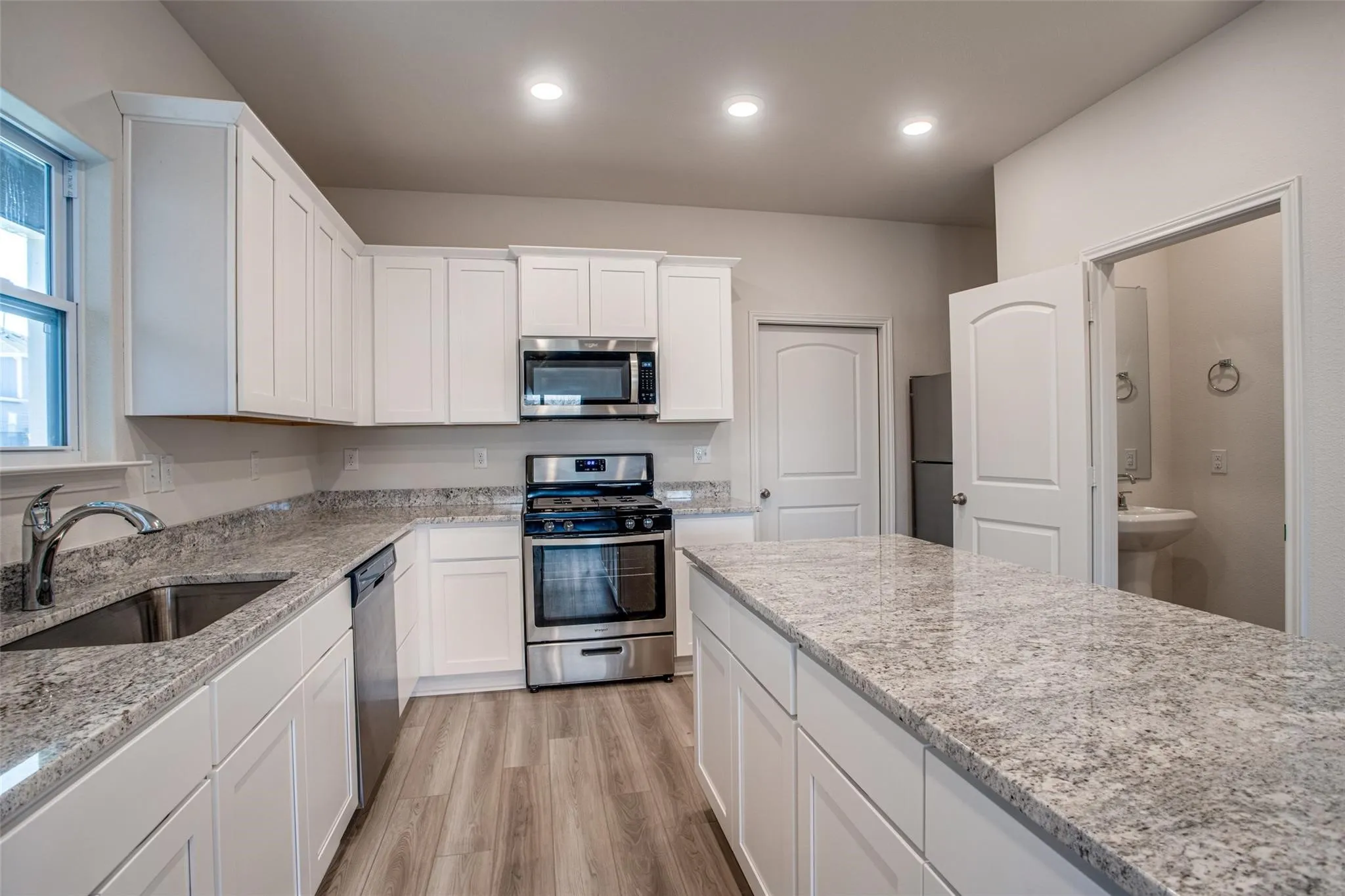 Kitchen featuring white shaker cabinetry, stainless steel appliances, speckled countertops, wood-finish flooring, and recessed lighting