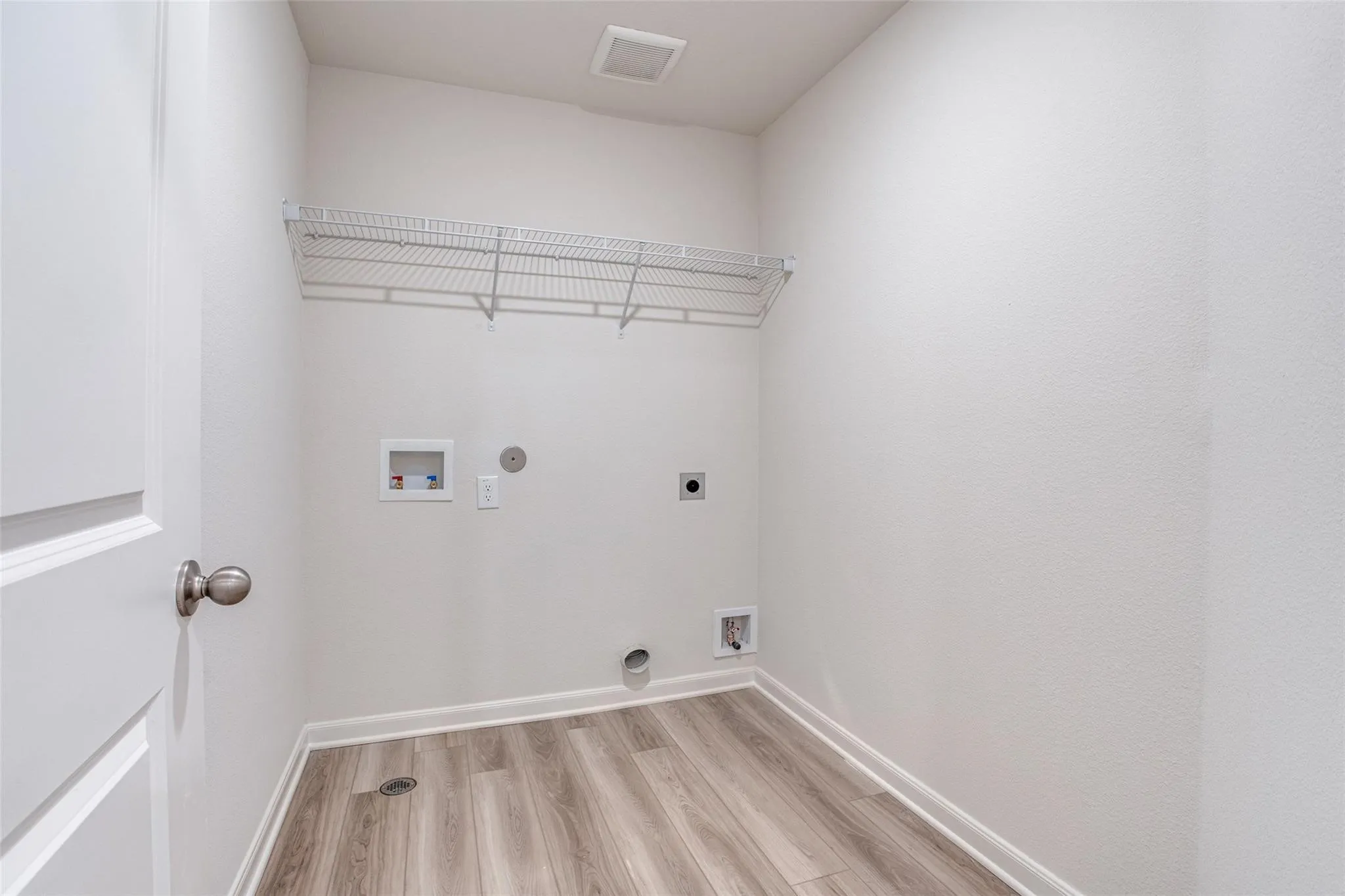 Dedicated laundry area featuring wood-finish flooring and a wire shelving unit