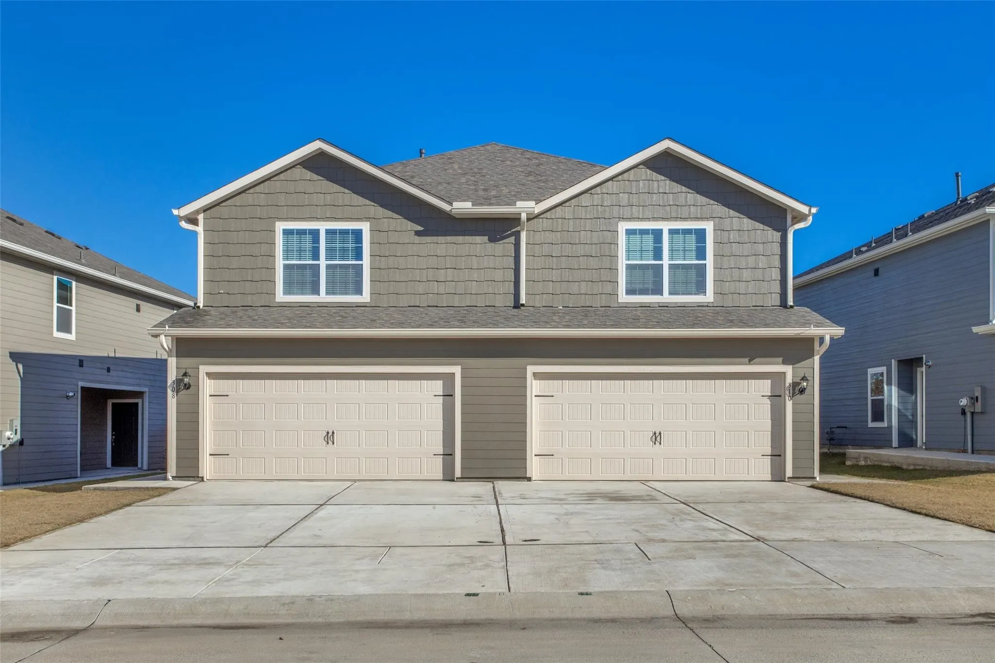 Duplex property with gray siding and shingle accents, two attached garages, and a paved driveway
