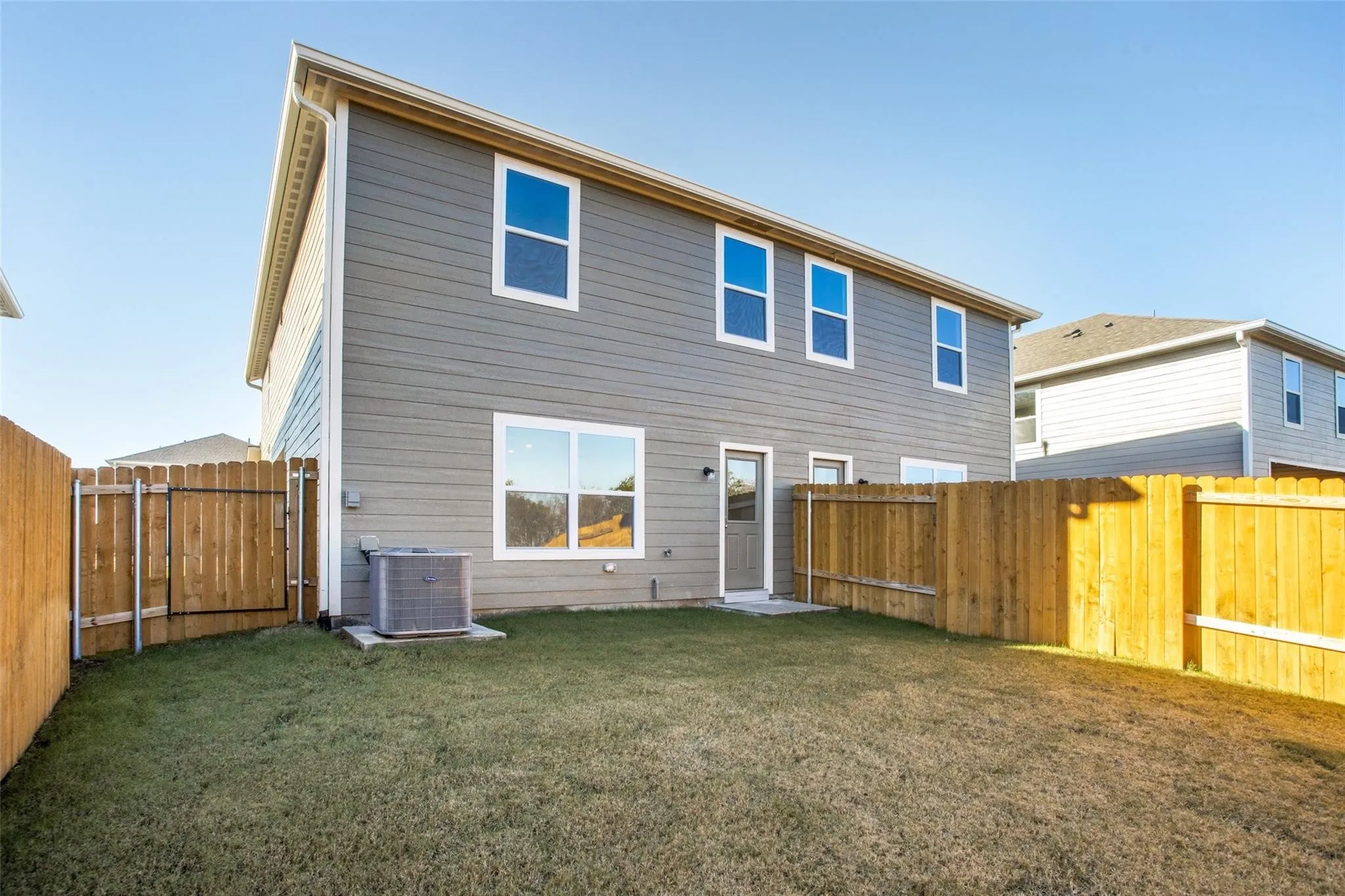 Exterior featuring grey horizontal siding, white trim windows, a rear entry door, and a concrete patio