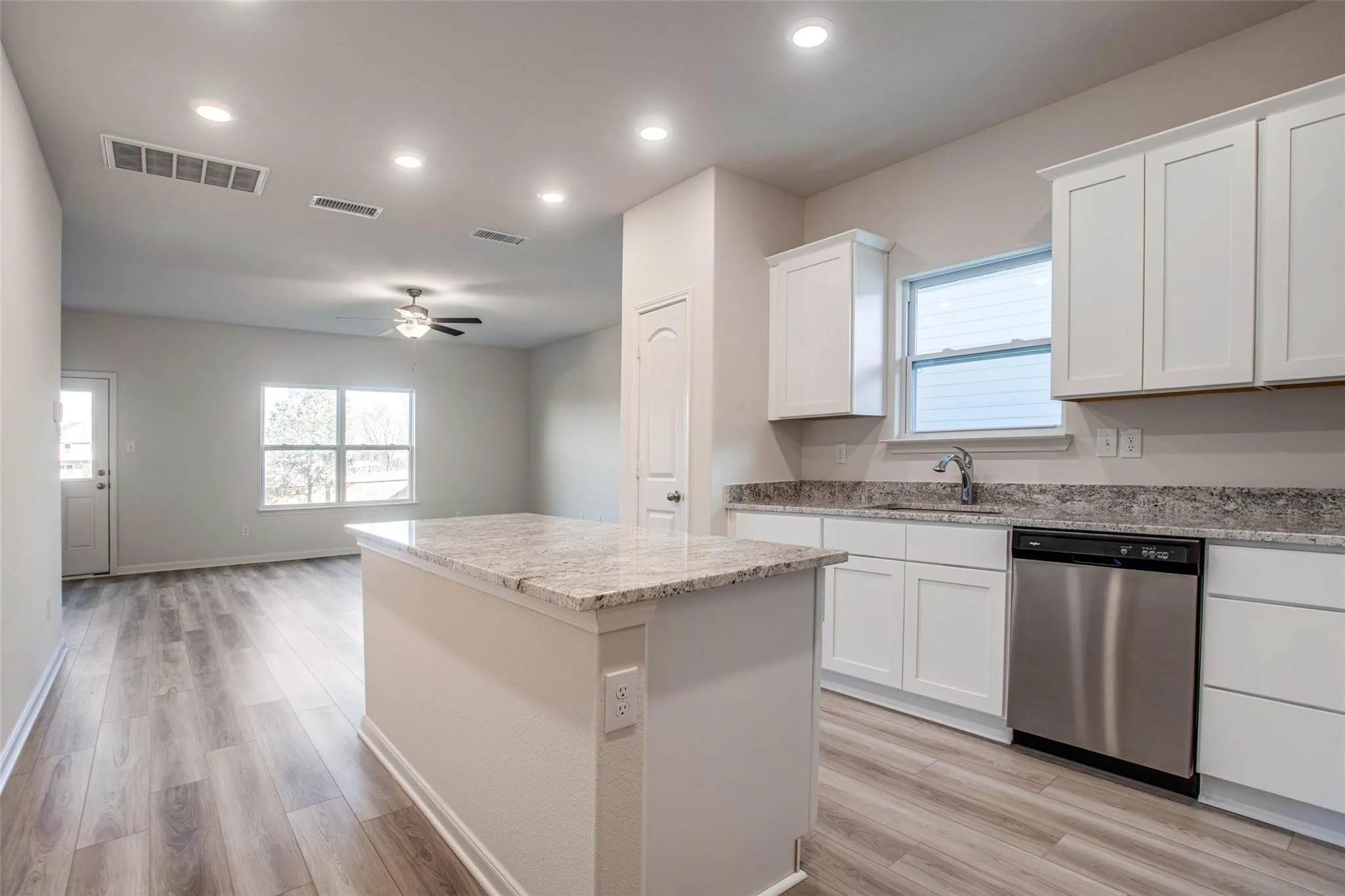 Kitchen with white cabinetry, stainless steel dishwasher, and granite countertops