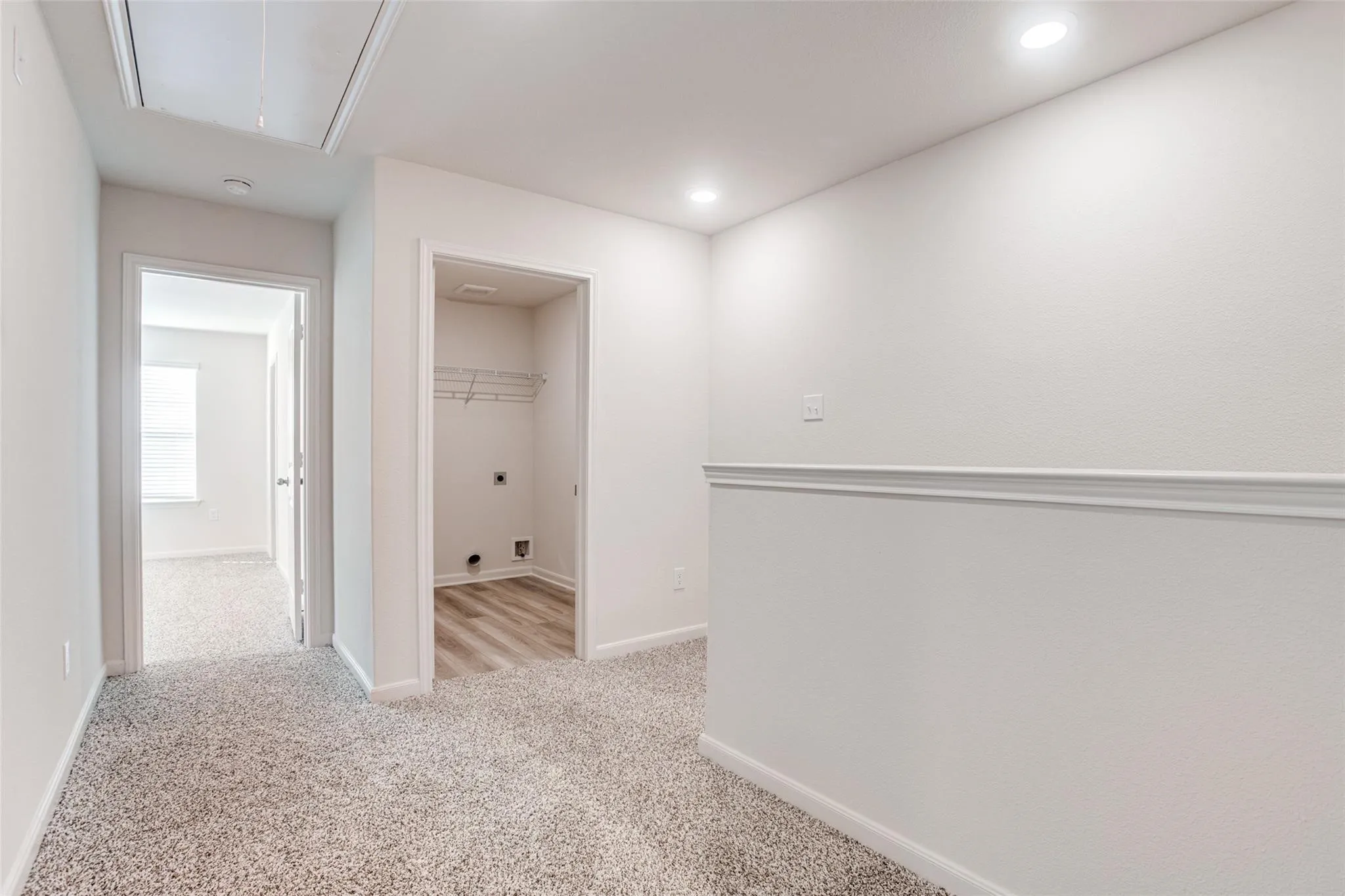 Carpeted hallway with a laundry area featuring wood-finish flooring, wire shelving, and overhead lighting
