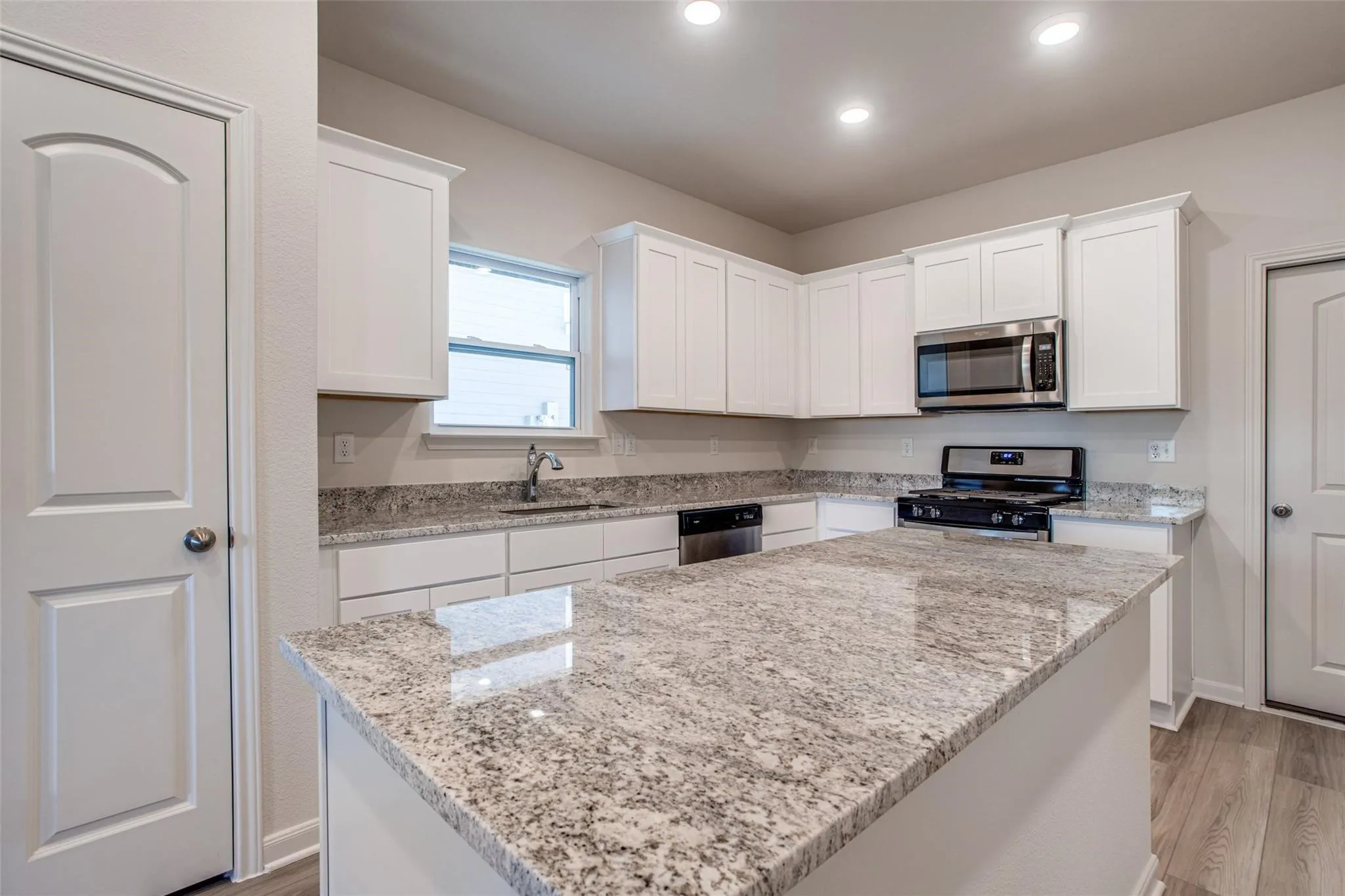 Kitchen featuring a central island with a granite countertop, white cabinetry, stainless steel appliances, and wood-finish flooring