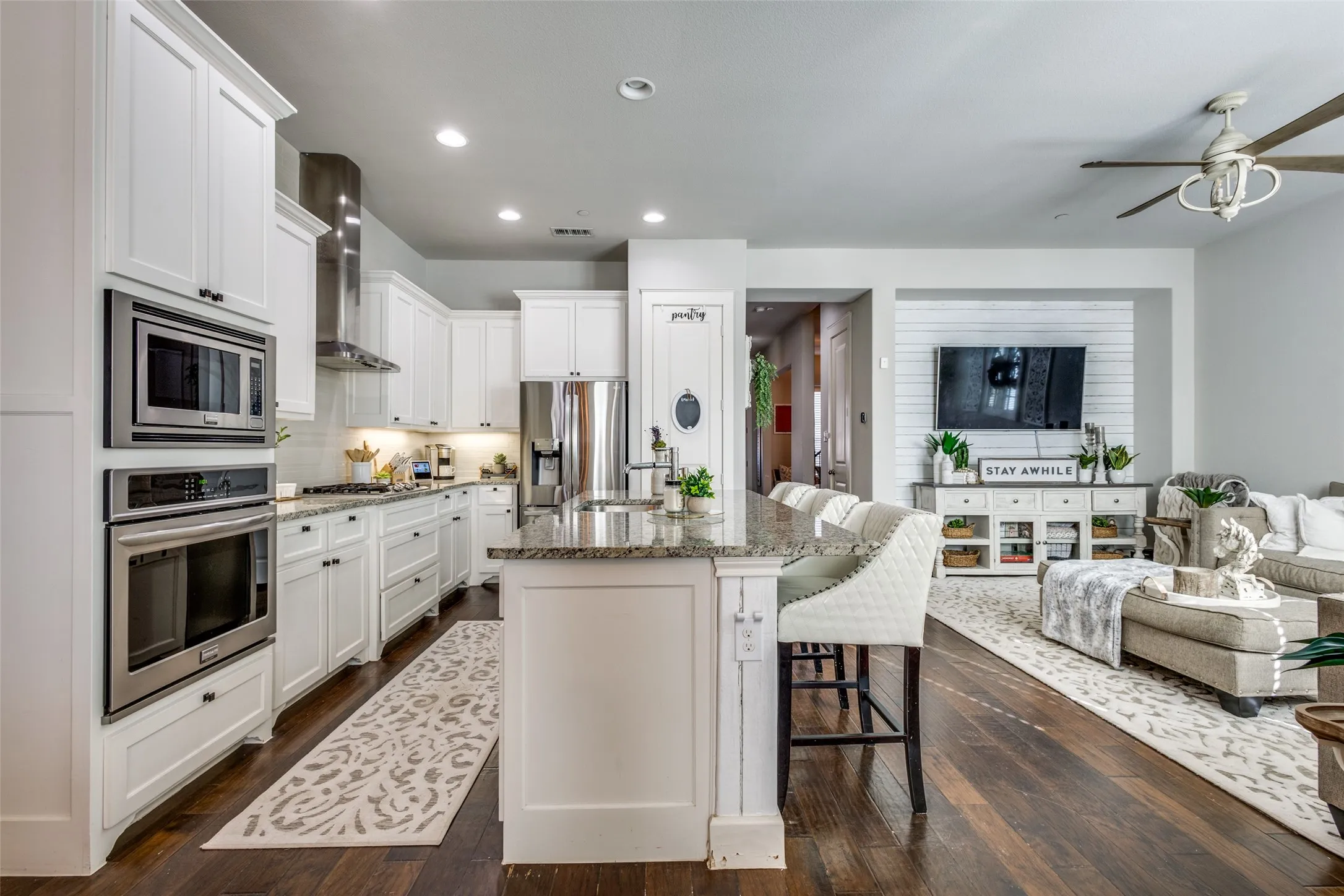 Open-concept living area featuring dark wood-finish flooring, white cabinetry, integrated stainless steel appliances, and a kitchen island with stone countertop