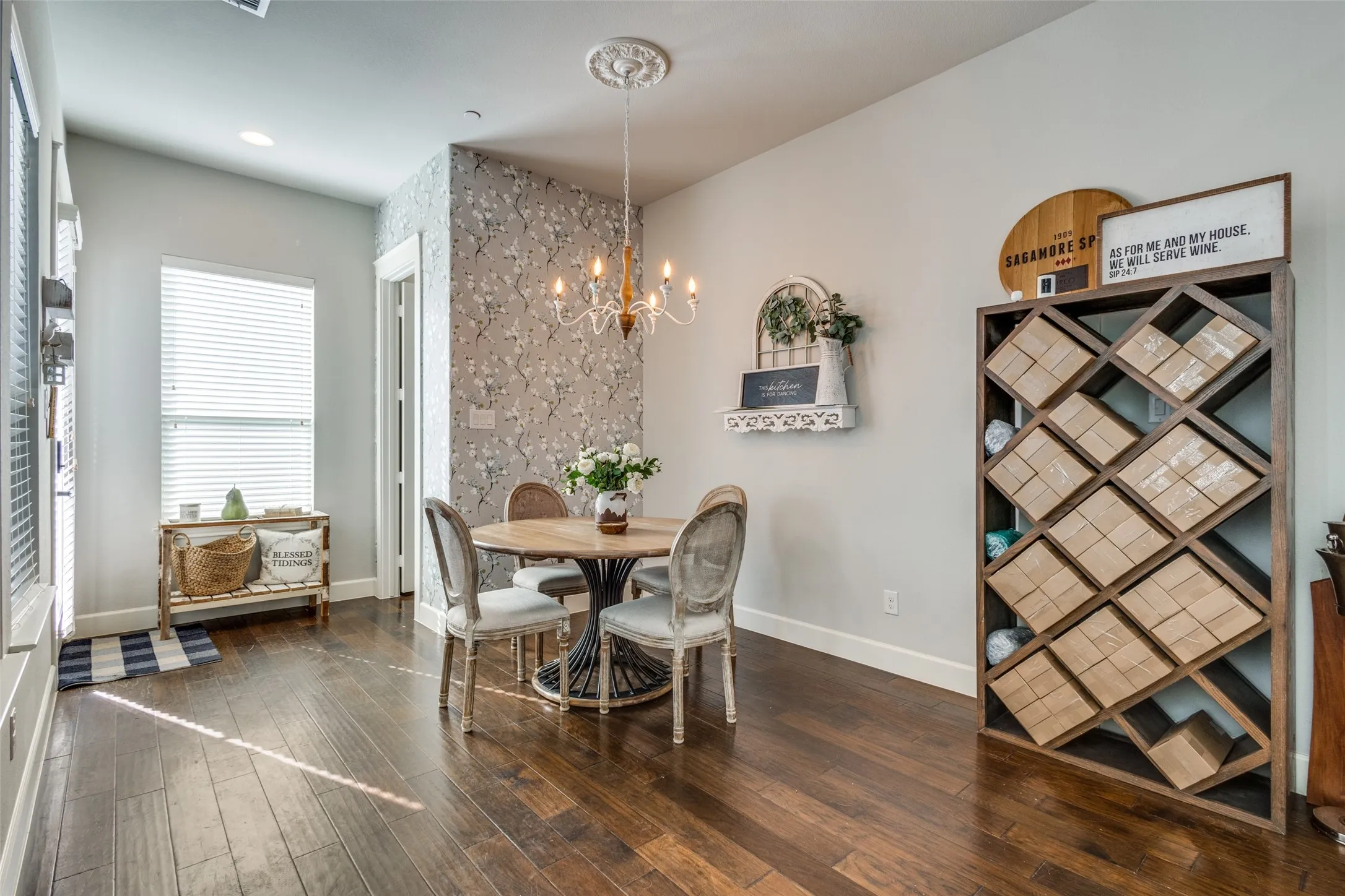 Hardwood-finish flooring, accent wall with patterned wallpaper, built-in shelving unit, and a window with blinds