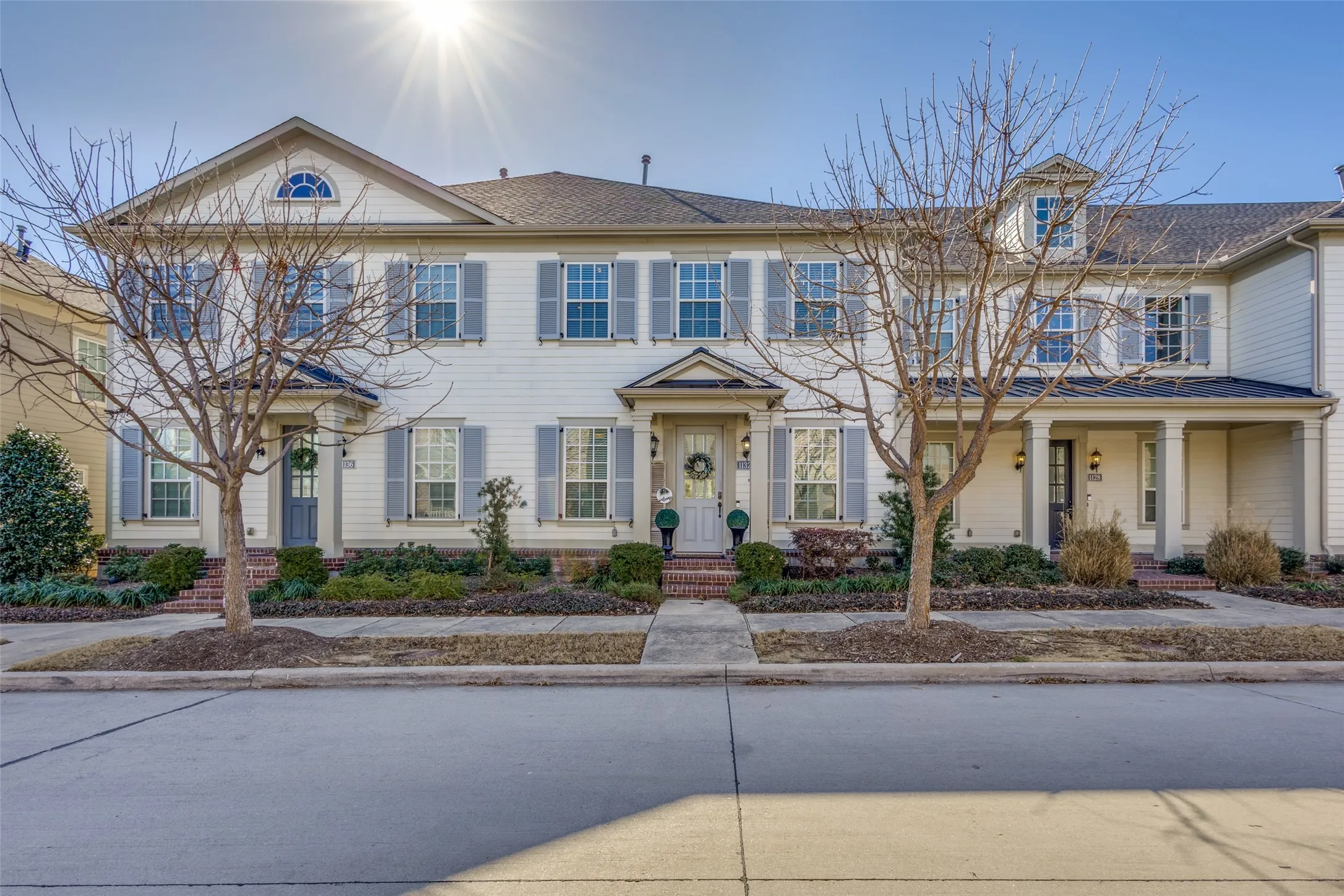Exterior featuring light-colored siding, contrasting shutters, covered front entryways, and manicured landscaping