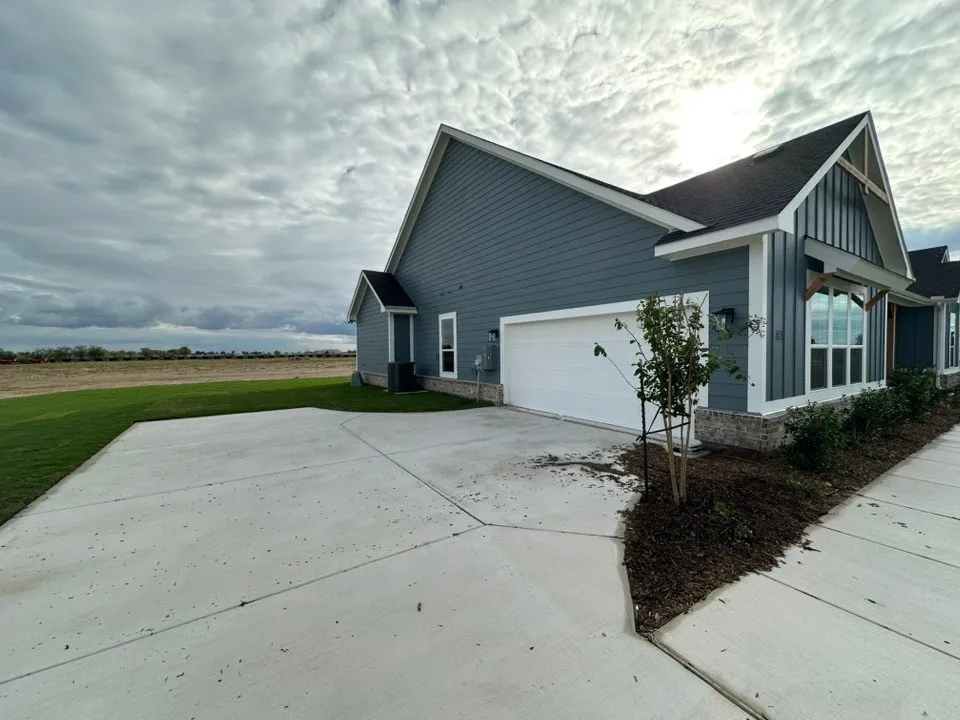 Contemporary siding exterior with a prominent gable, attached garage, concrete driveway, and landscaped shrubbery