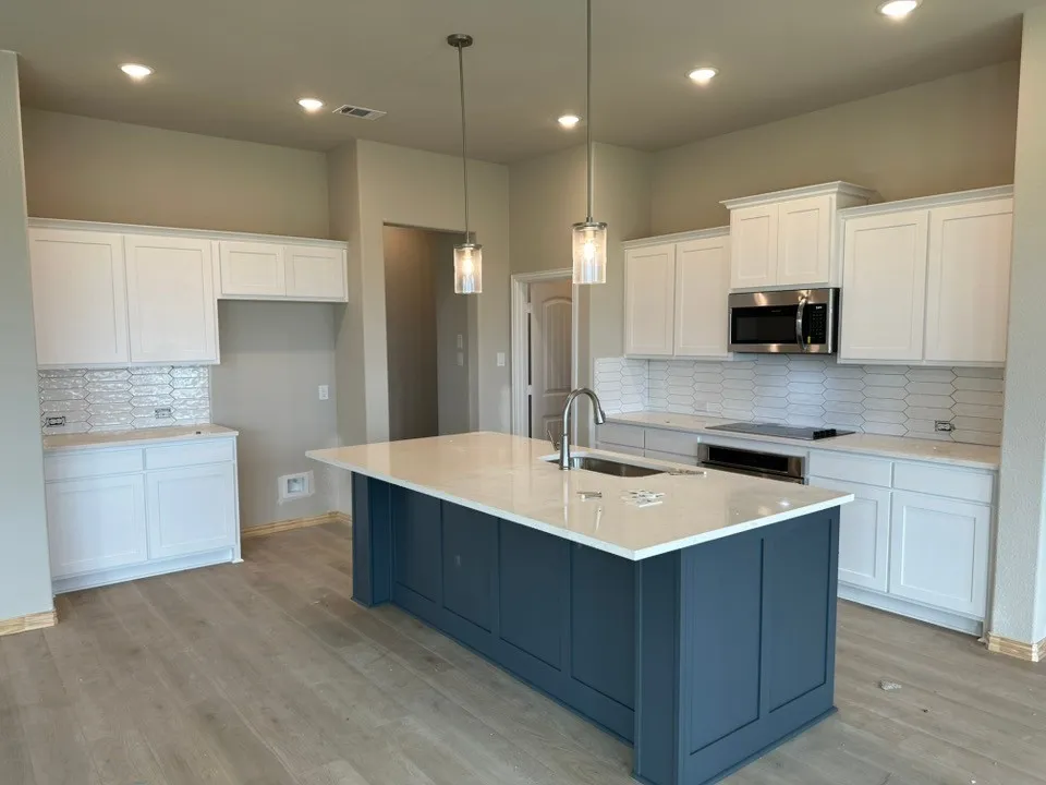 Kitchen featuring a blue shaker-style island, white cabinetry, integrated stainless steel microwave, white elongated subway tile backsplash, and light wood-finish flooring