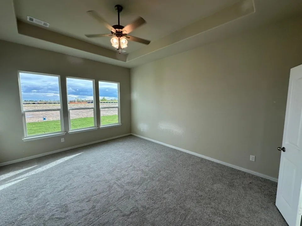 Bright corner bedroom with triple-window exposure overlooking expansive grounds, neutral wall finishes, ceiling fan with integrated lighting, and neutral carpet flooring throughout