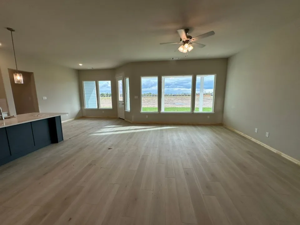 Expansive room featuring wood-finish flooring, a contemporary ceiling fan, recessed lighting, a built-in kitchen island with dark cabinetry, and multiple windows providing ambient light