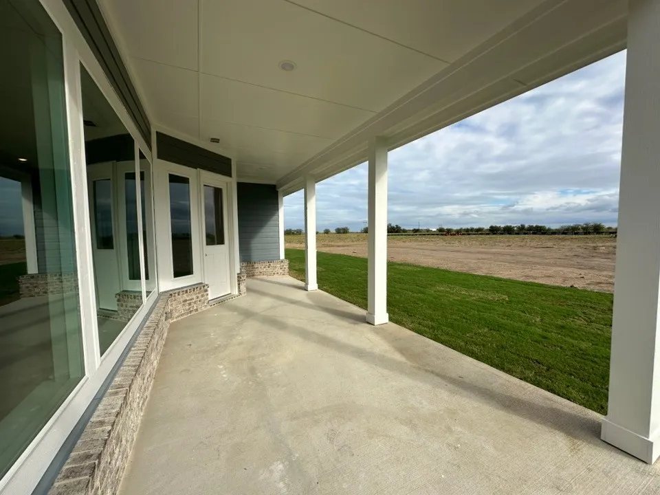 Expansive covered patio with concrete flooring, brick wainscoting, and white support columns