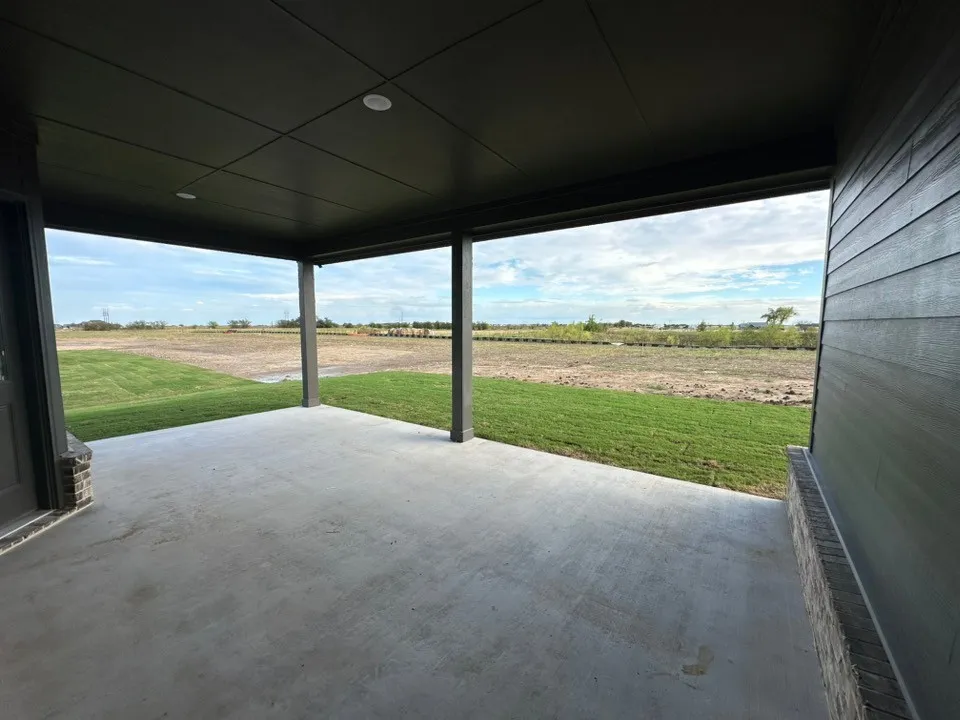 Covered concrete patio with recessed lighting, supported by columns, and an exterior wall featuring horizontal siding and stone detailing